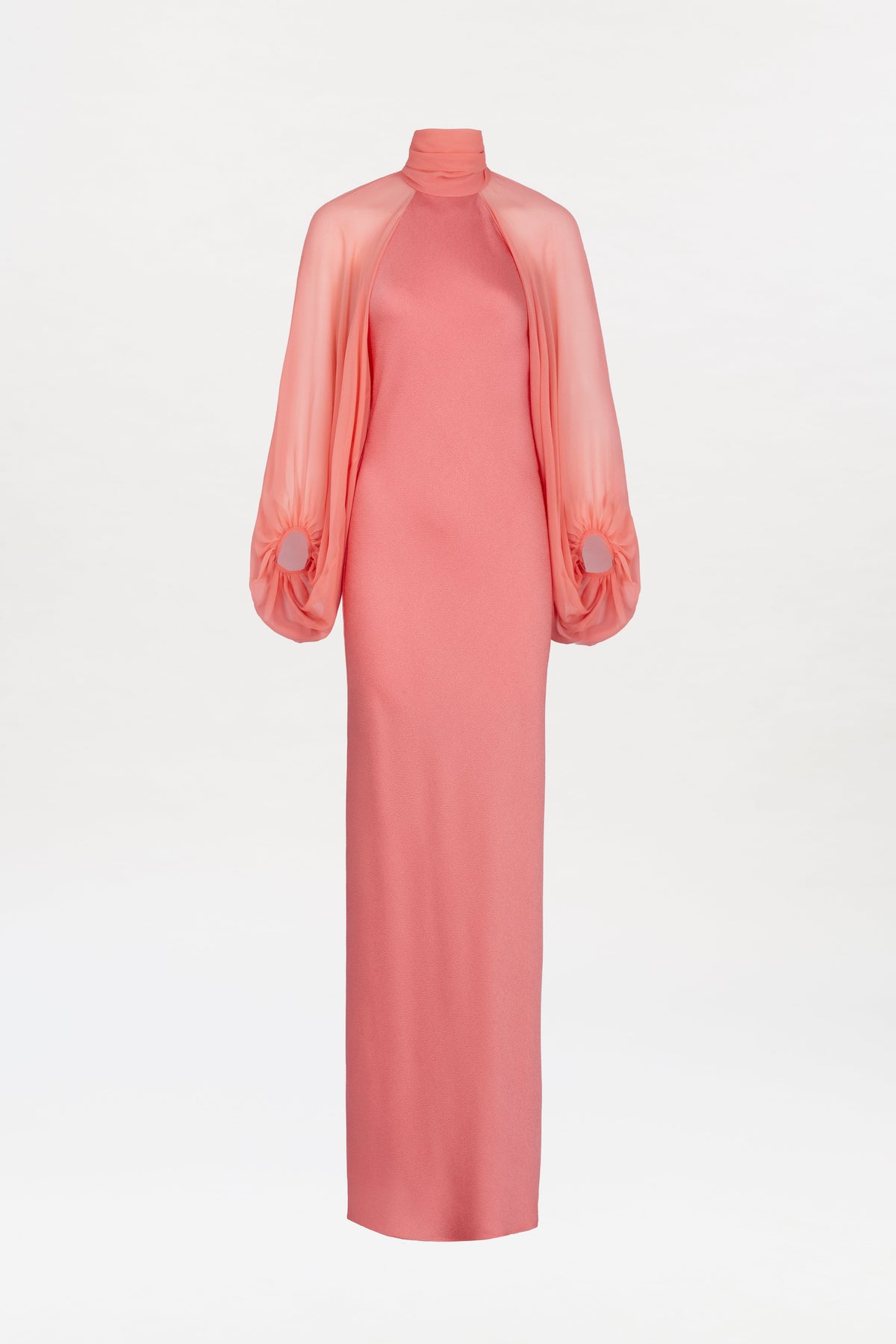 The Martine Dress is a coral pink, floor-length gown featuring a high neckline, long sheer sleeves gathered at the wrists, and a fitted silhouette, displayed against a white background.