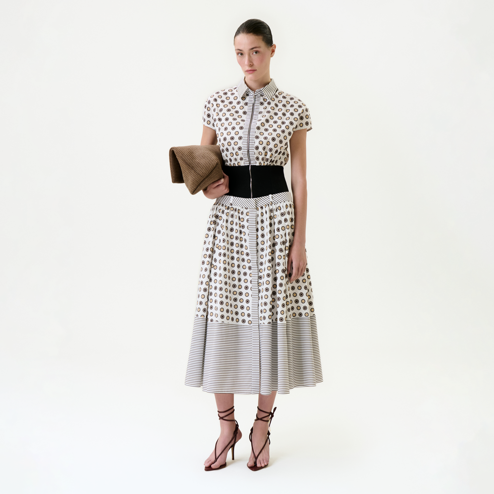 Woman wearing a patterned dress holding a clutch on a white background