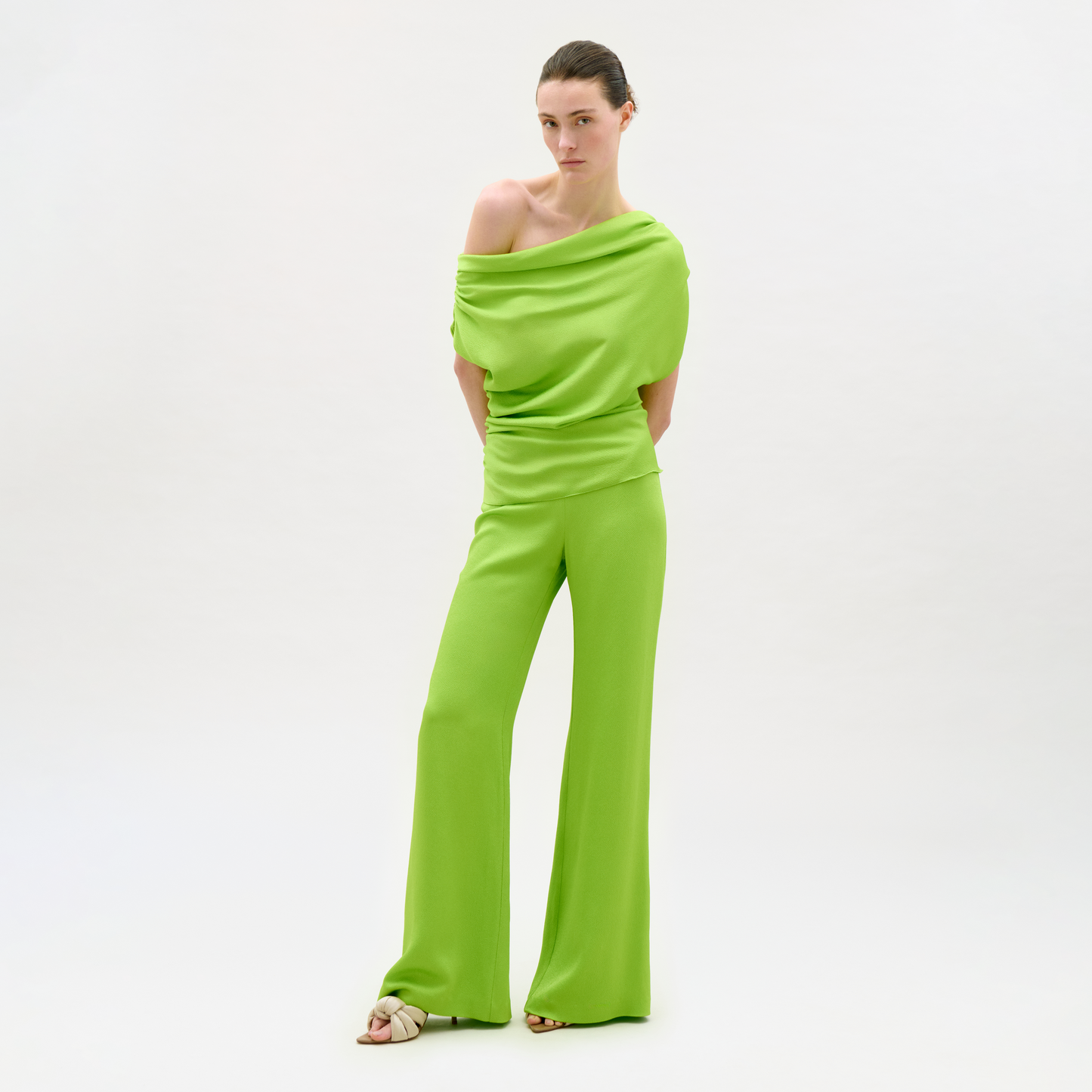 Woman wearing a bright green off-shoulder jumpsuit on a white background