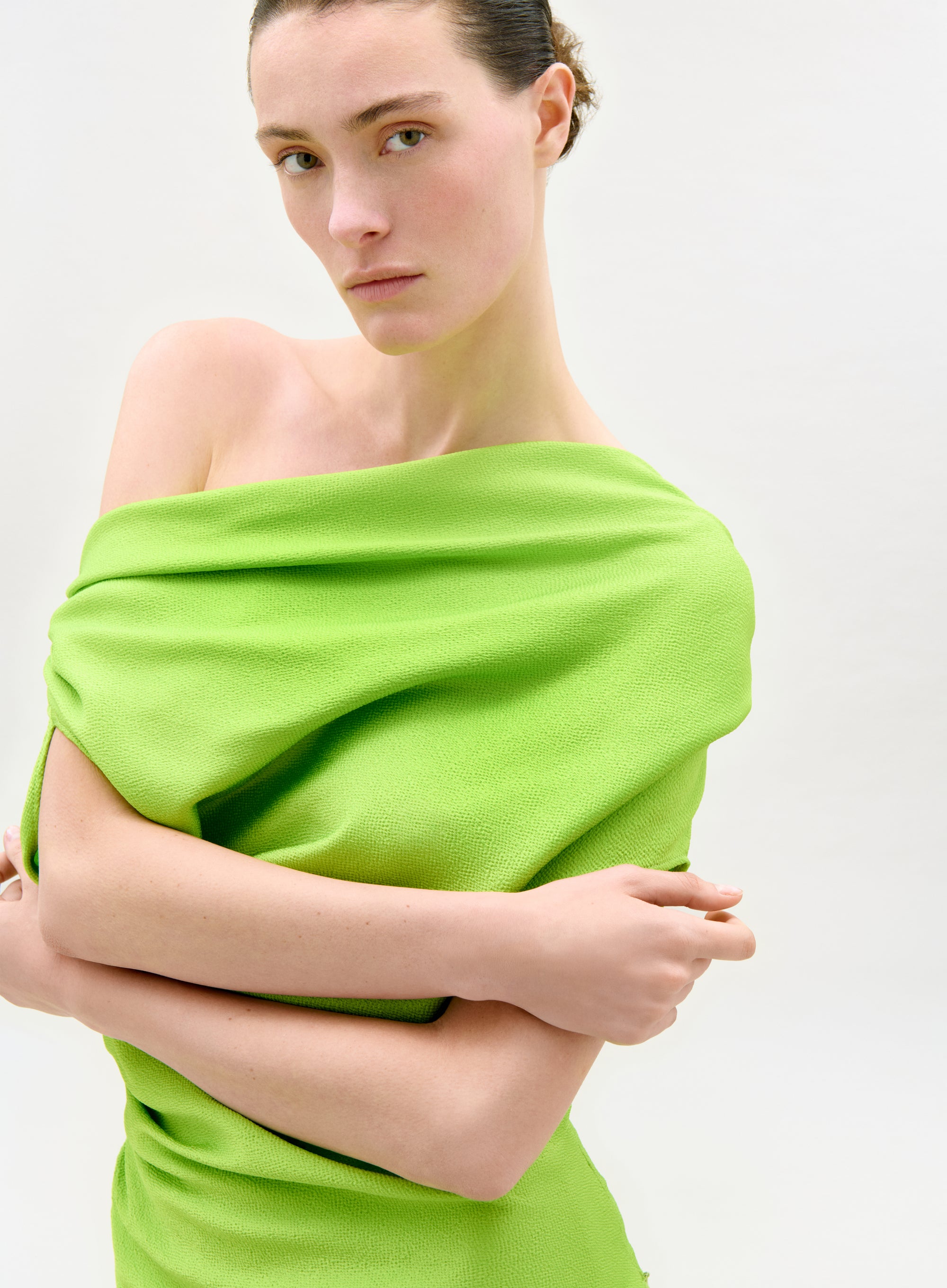 Woman wearing a bright green off-shoulder top against a white background