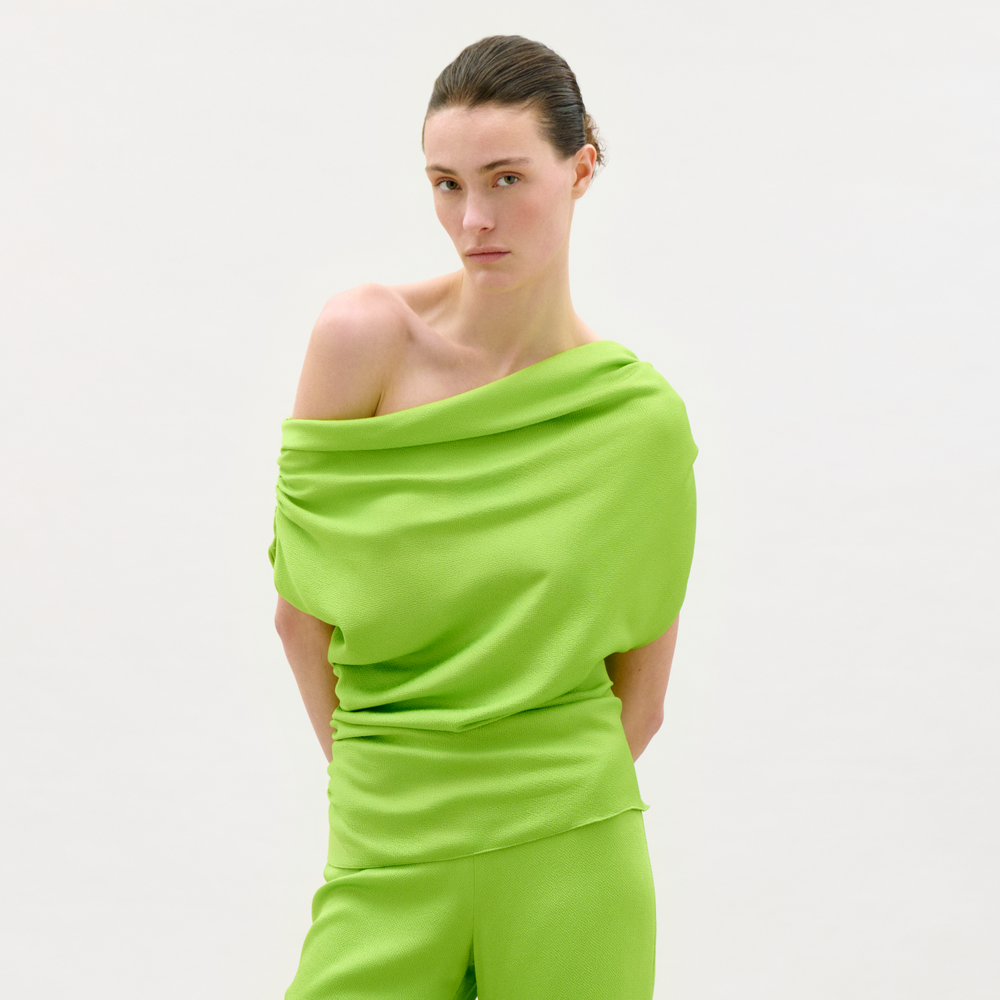 Woman wearing a bright green off-shoulder top and pants on a white background