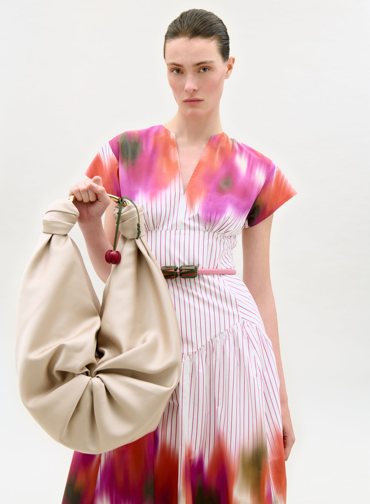 Woman holding a beige bag wearing a colorful dress on a white background