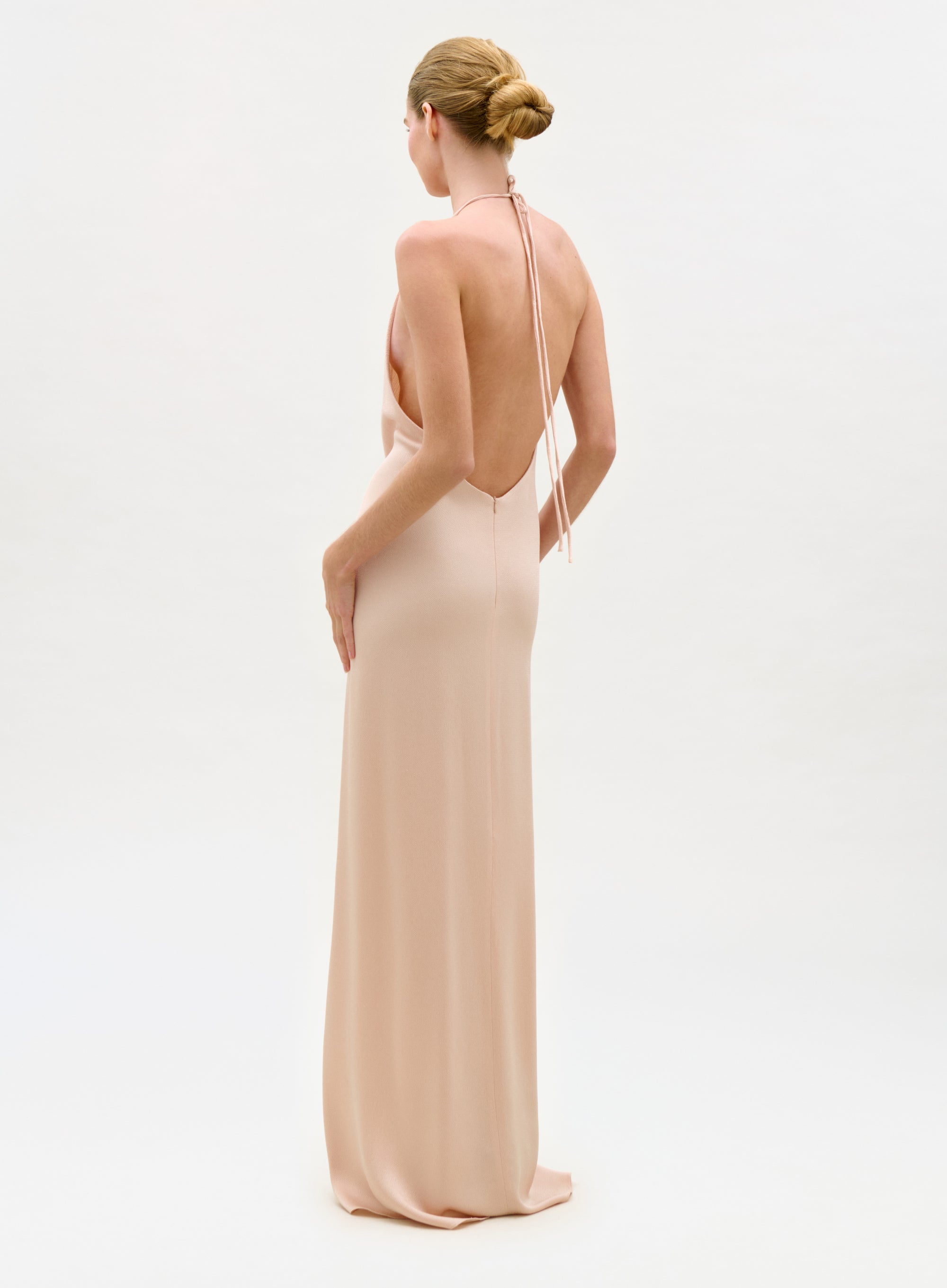 Woman wearing a long, elegant dress with thin straps on a plain background