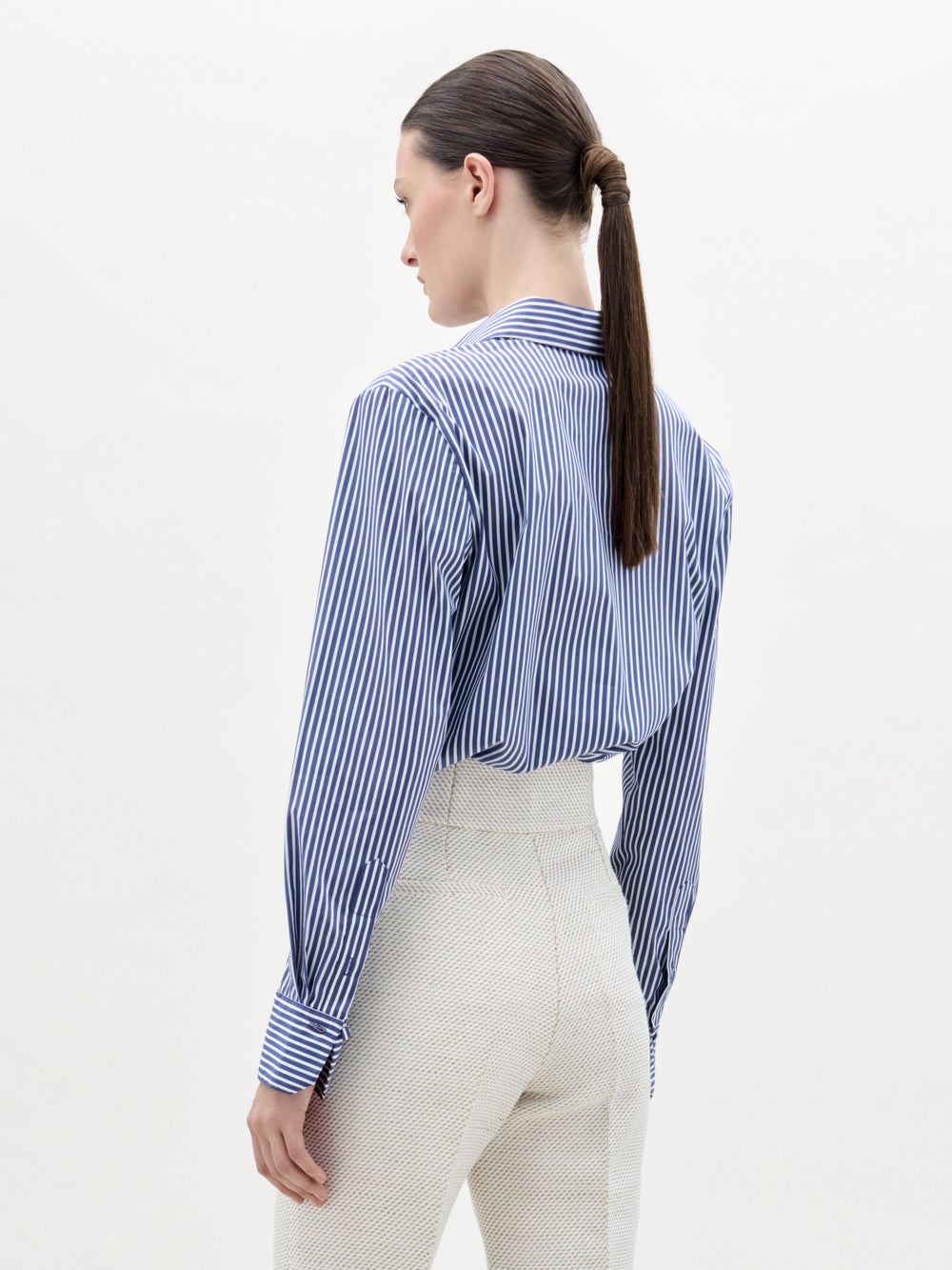 A woman with a ponytail wears the Karole Blouse, a striped button-down shirt crafted from Italian fabric.