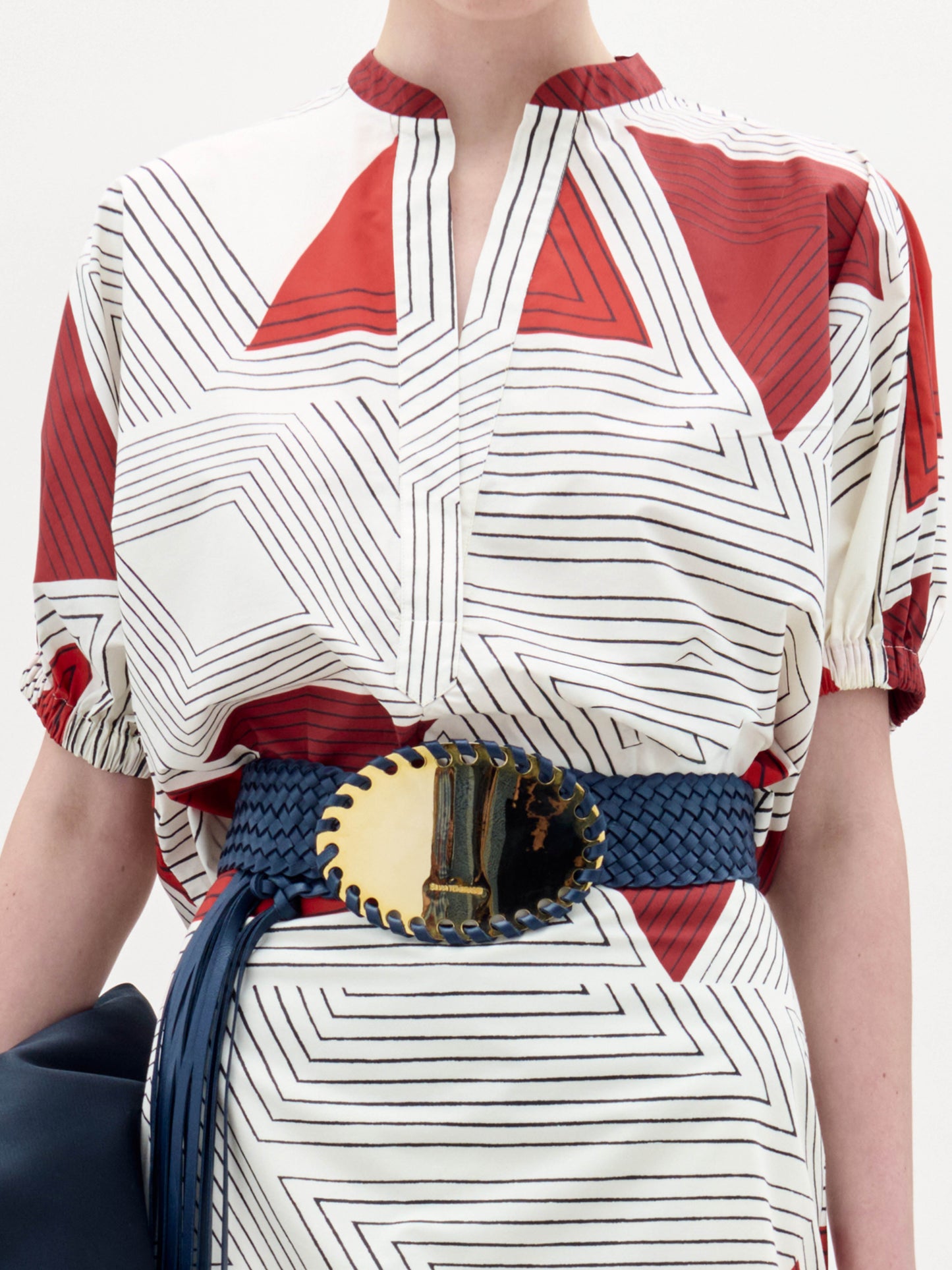 Woman standing against a plain background, wearing the Susanne Blouse and holding a black clutch.
