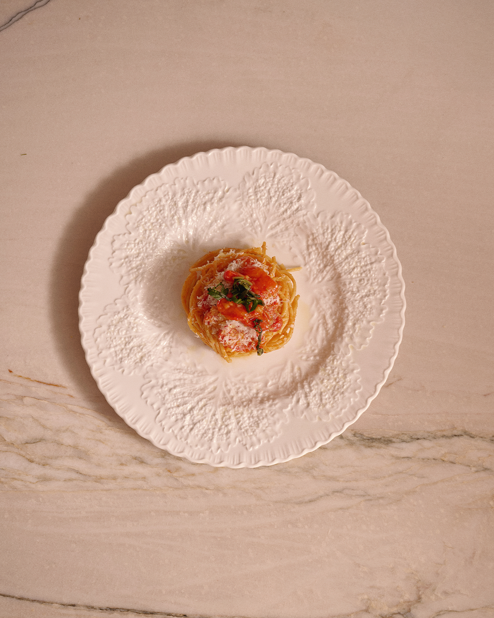 Small dish of pasta with vegetables on a textured white plate on a marble surface