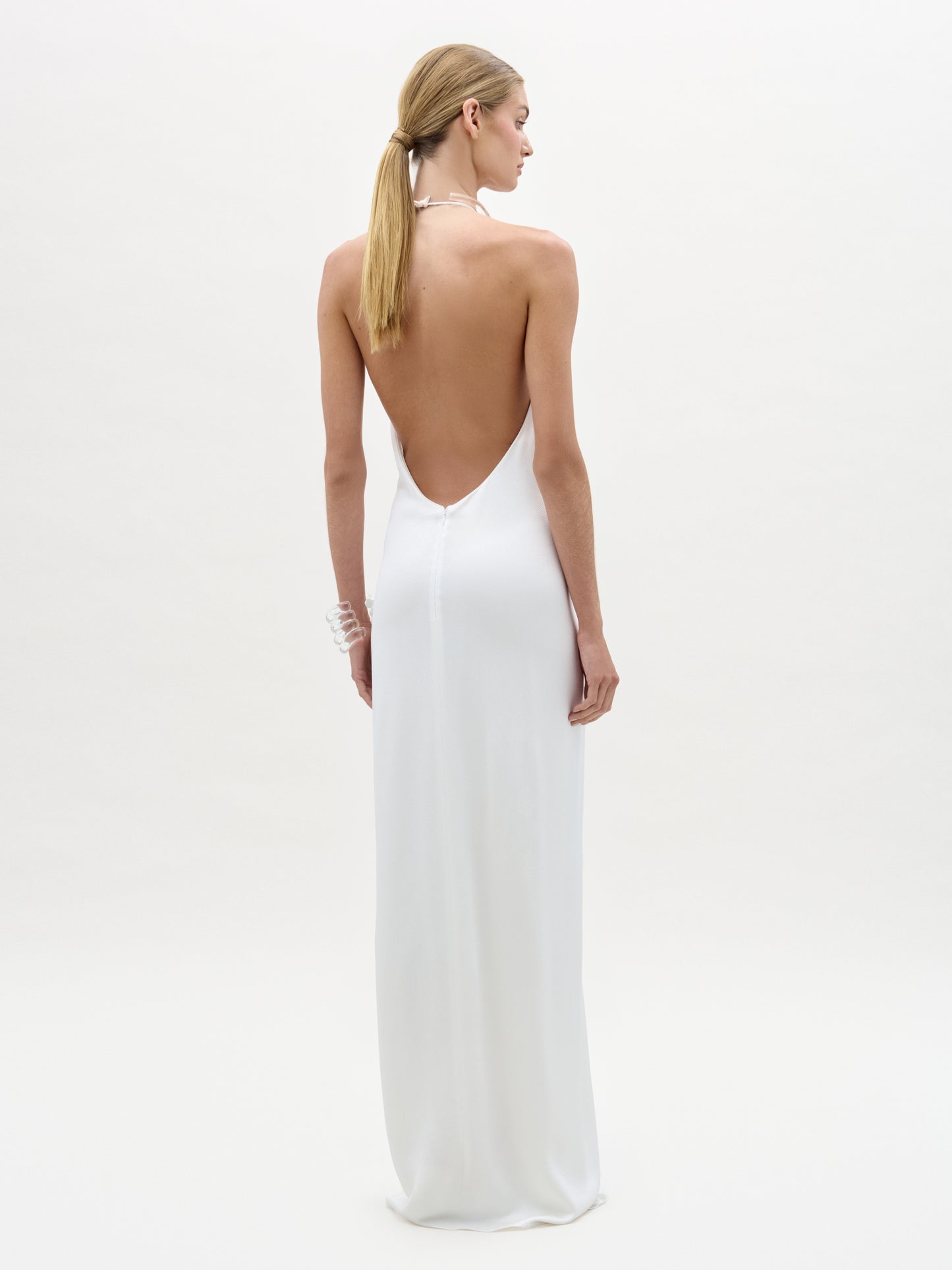 Woman wearing a white dress with an open back on a plain background