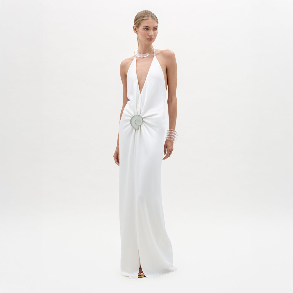 Woman wearing a white halter neck gown with a decorative brooch on a white background