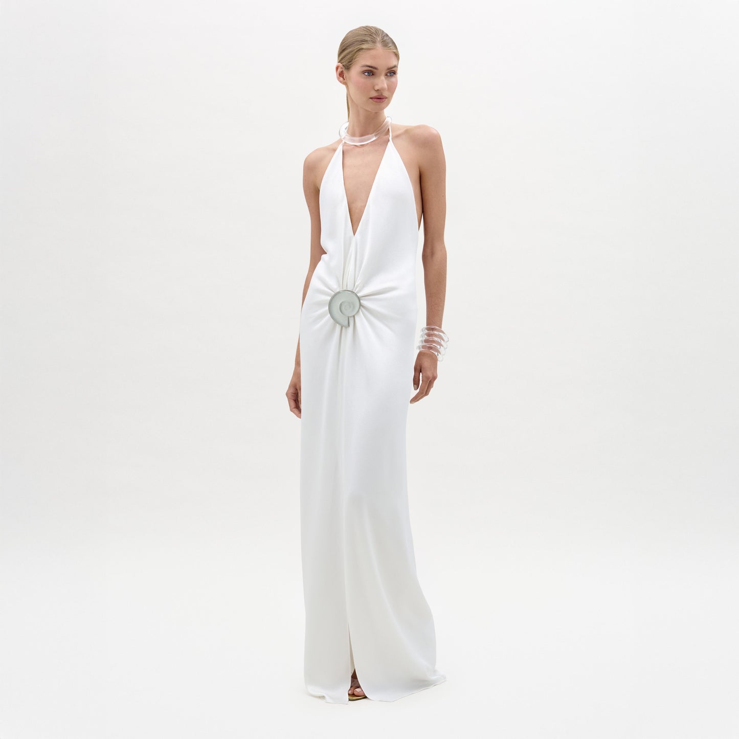 Woman wearing a white halter neck gown with a decorative brooch on a white background