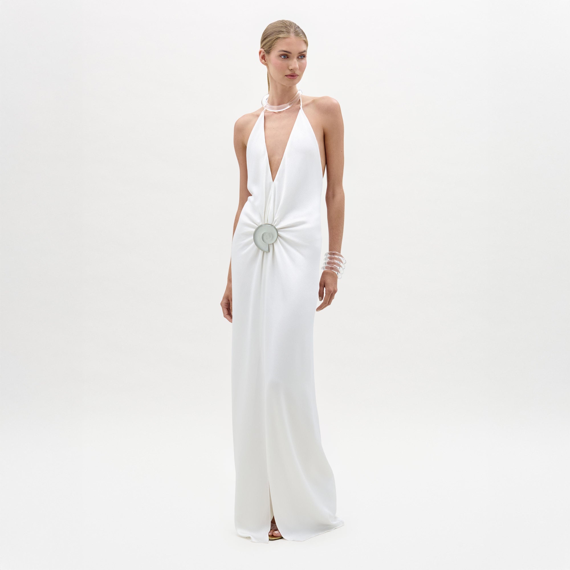 Woman wearing a white halter neck gown with a decorative brooch on a white background