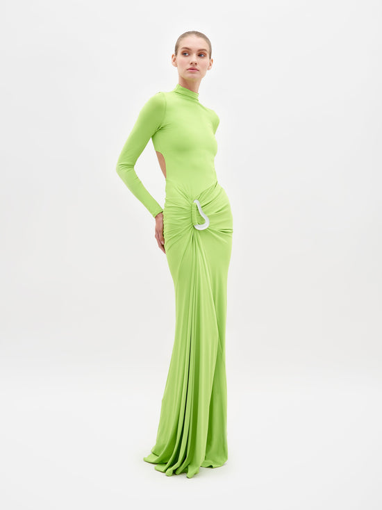 A person is wearing the Lena Dress Lime, a long, lime green dress with long sleeves and a high neckline. The dress, which is available for shipping by February 15th, features cut-out details at the sides and a gathered, draped front. White background.