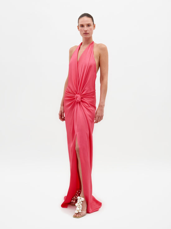 A person wearing the Torgiano Dress Peony, which features a sleeveless, V-neck design with a knot detail at the front and a slit, standing against a plain white background. Pre-order now to ensure delivery by February 15th, 2025.