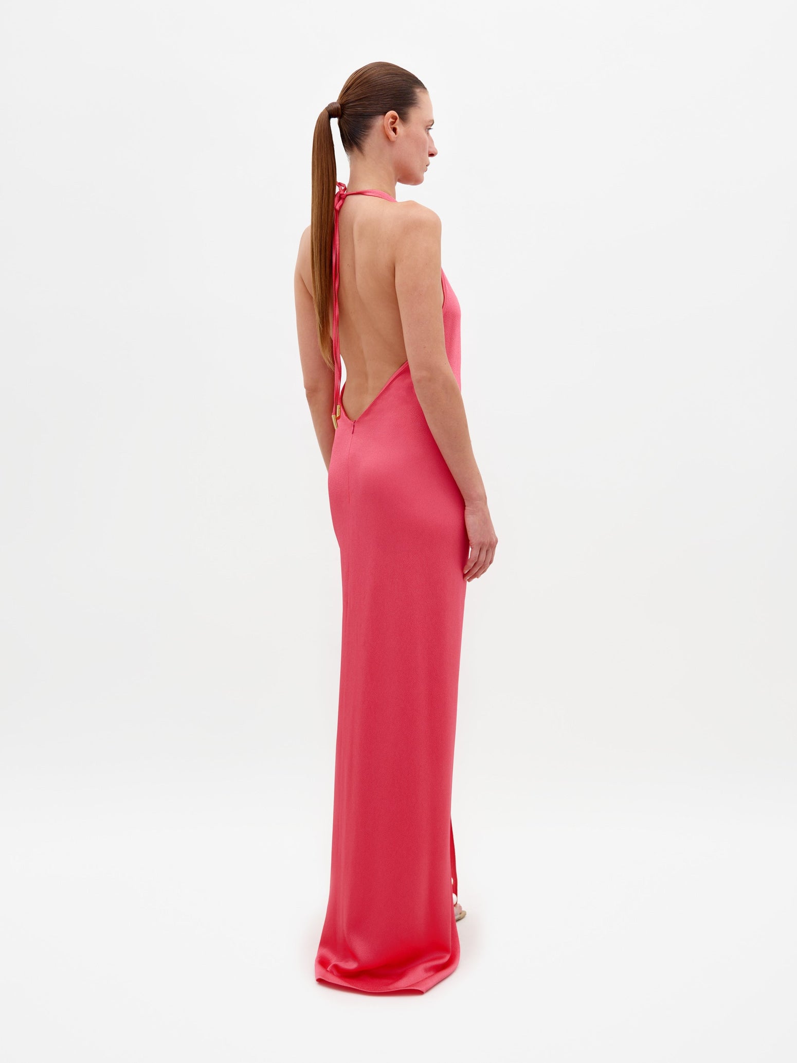 A person wearing the Torgiano Dress Peony, which features a sleeveless, V-neck design with a knot detail at the front and a slit, standing against a plain white background. Pre-order now to ensure delivery by February 15th, 2025.