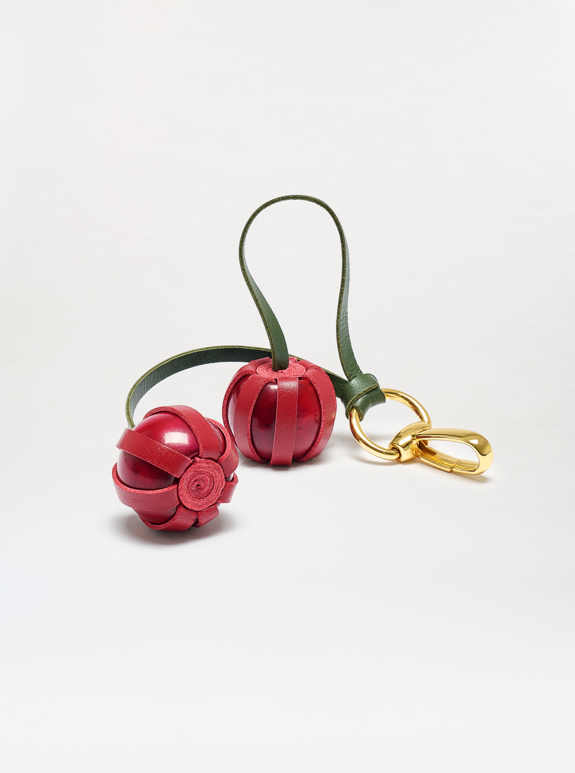 The Candy Charm keychain features two red, spherical, flower-like leather charms with an olive green strap and a gold metal clasp, shown on a white background.