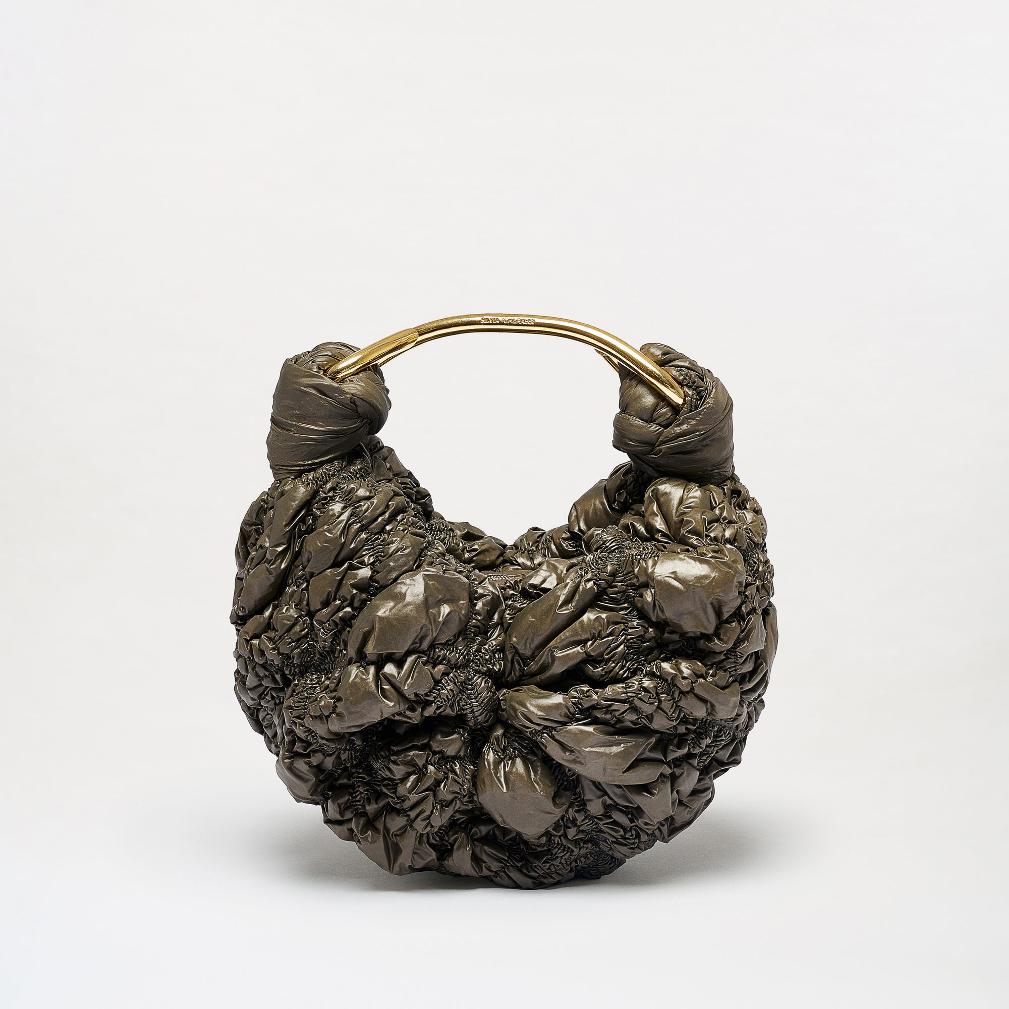 The Sofia Bag (Small) features a gold-toned circular handle and a dark, textured surface reminiscent of gathered plastic or fabric. Crafted from luxurious Italian fabric and made in Colombia, it is presented against a plain white background.