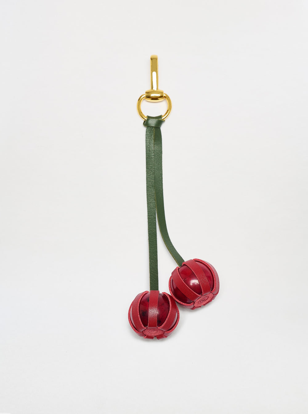 The Candy Charm features a gold keyring with a green leather strap and two decorative red leather balls, shown against a plain white background.