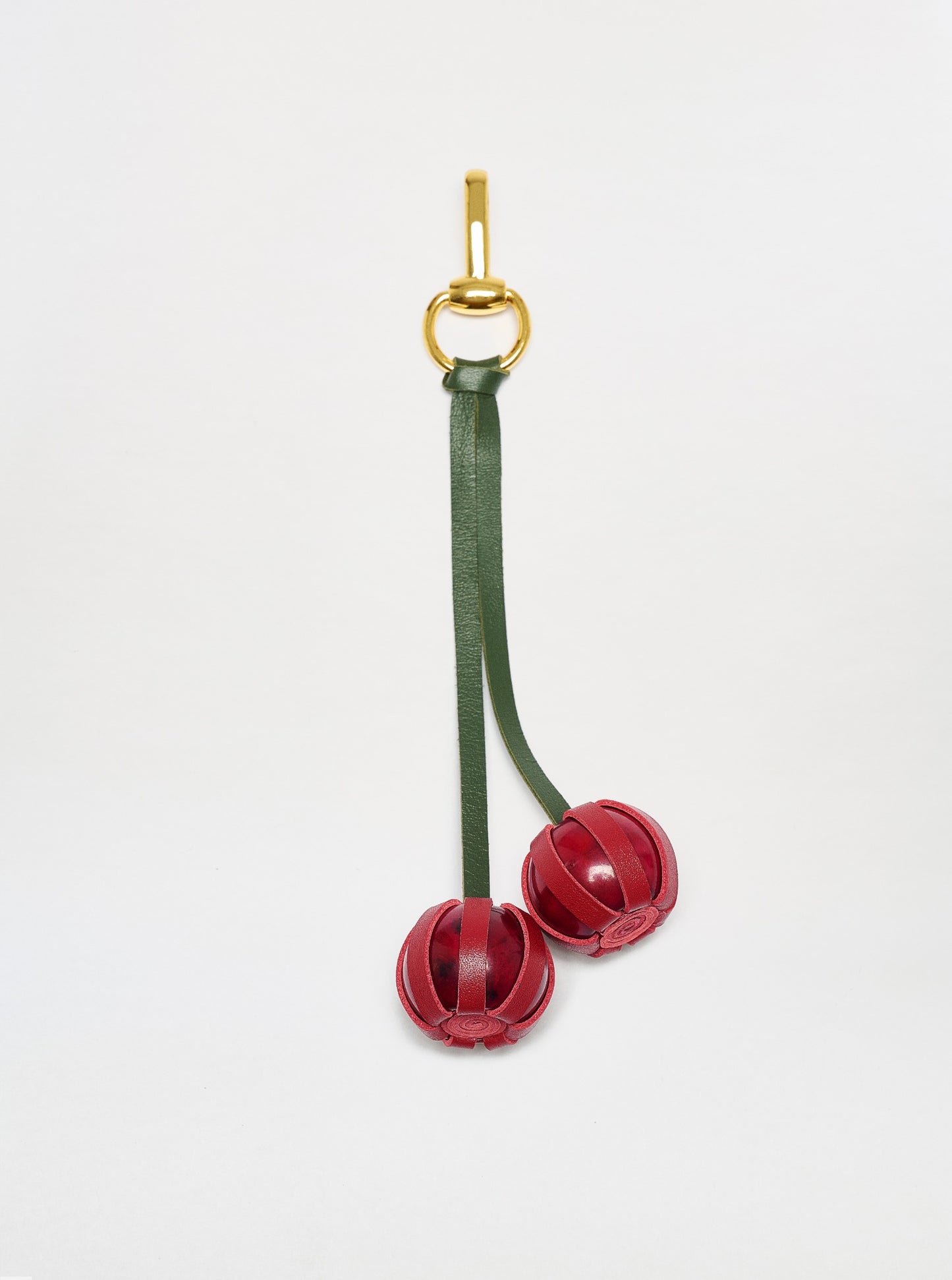 The Candy Charm features a gold keyring with a green leather strap and two decorative red leather balls, shown against a plain white background.