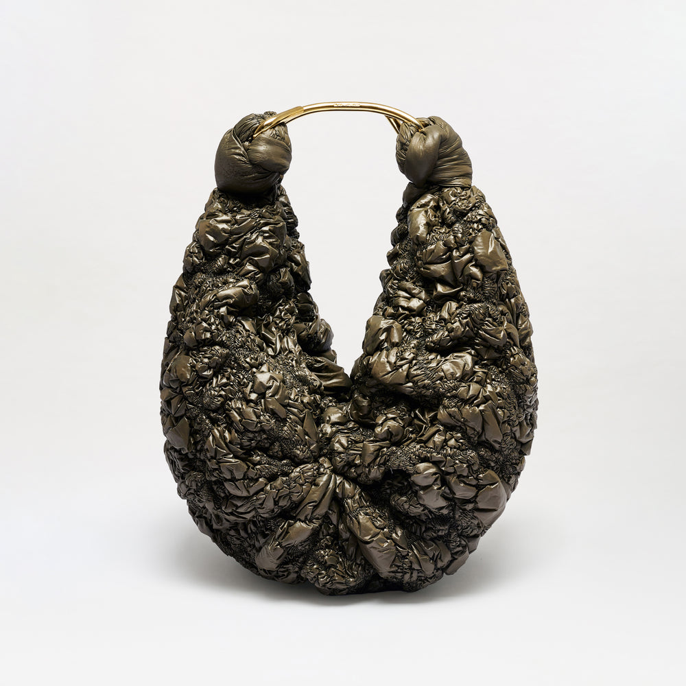 The Sofia Bag (Maxi), featuring a sculptural silhouette, dark textured material, gold-toned handle, and a twisted, crumpled design, sits upright against a plain white background.