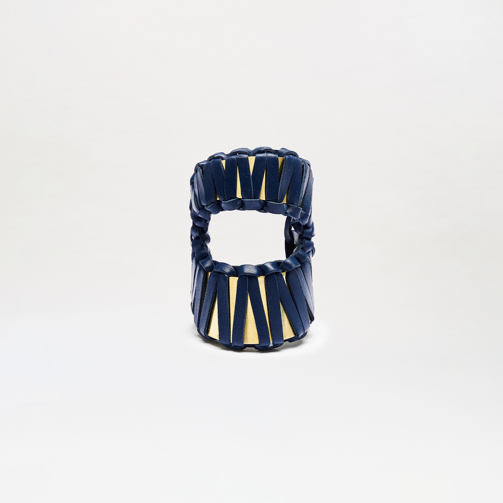 The Majel Cuff is a wide, circular bracelet with interwoven navy blue and gold bands, displayed upright against a plain white background.