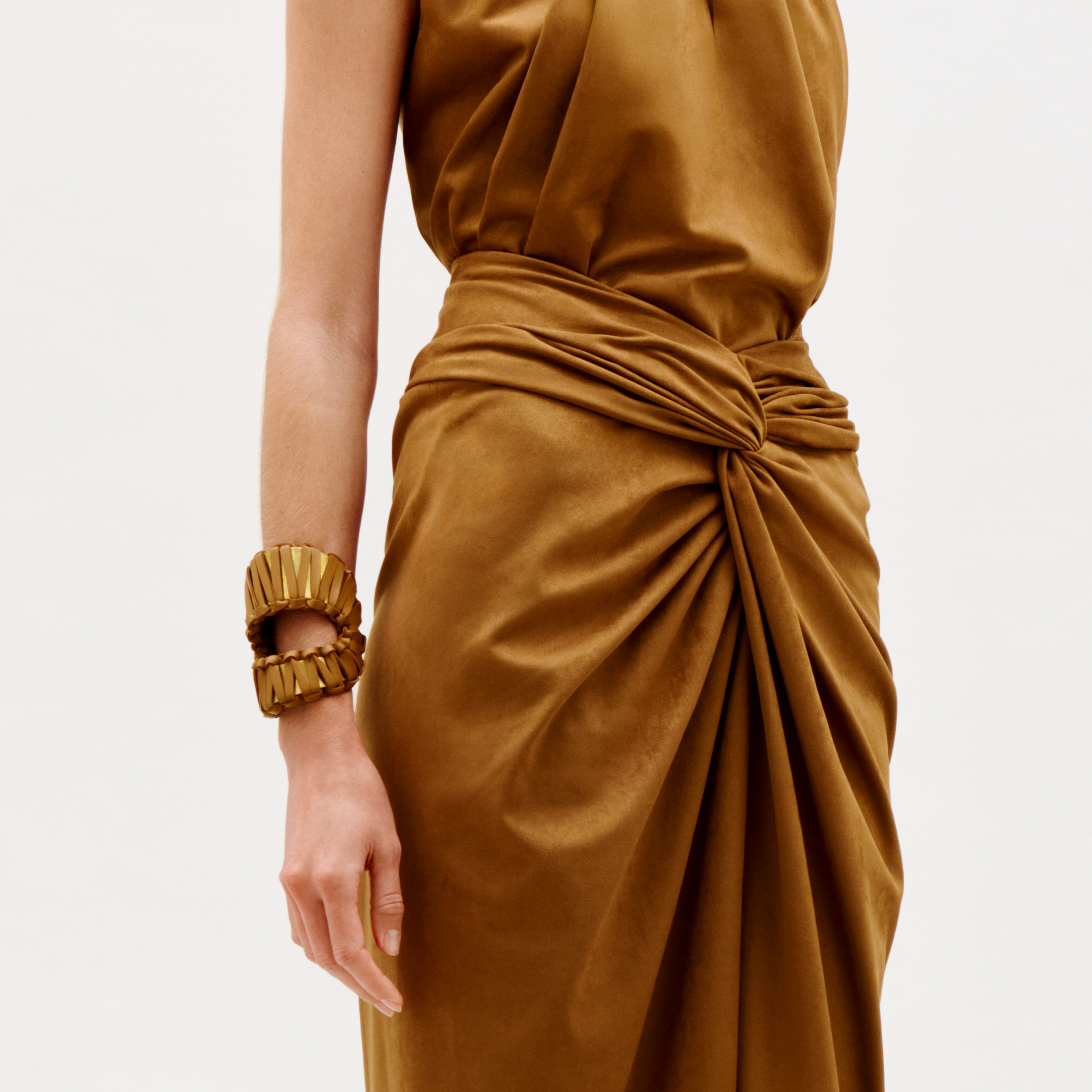 A person wears a brown satin dress with gathered waist details, accessorized with Majel Cuff chunky gold bracelets on their left wrist, standing against a plain white background.