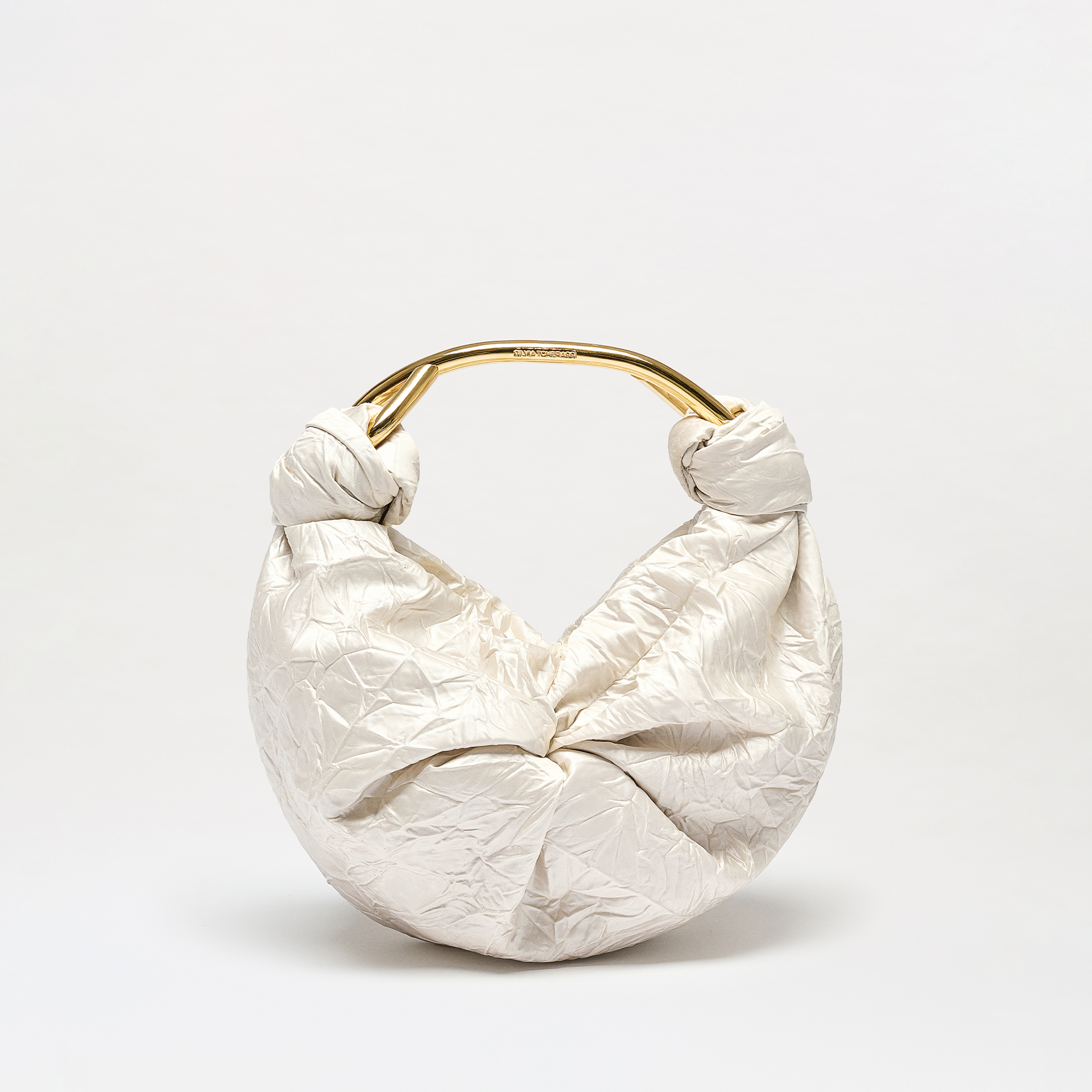 The Sofia Bag (Small) is a white bag with a crinkled texture, made from Italian fabric. It features a round gold-toned handle and knot details on both sides, shown against a plain white background.