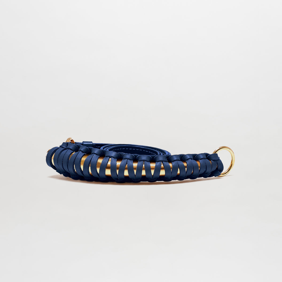 The Ife Belt is a coiled navy blue leather belt featuring gold metal rings at both ends, crafted in Colombia and displayed against a plain light background.