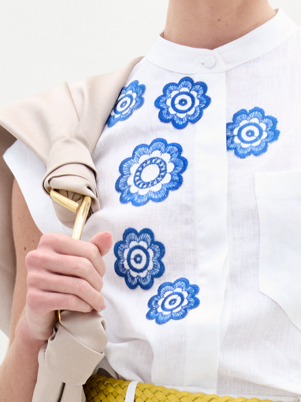 A person wearing the Adele Blouse in color White Navy Embroidery with a Sofia Bag Maxi in color Beige on a white background.