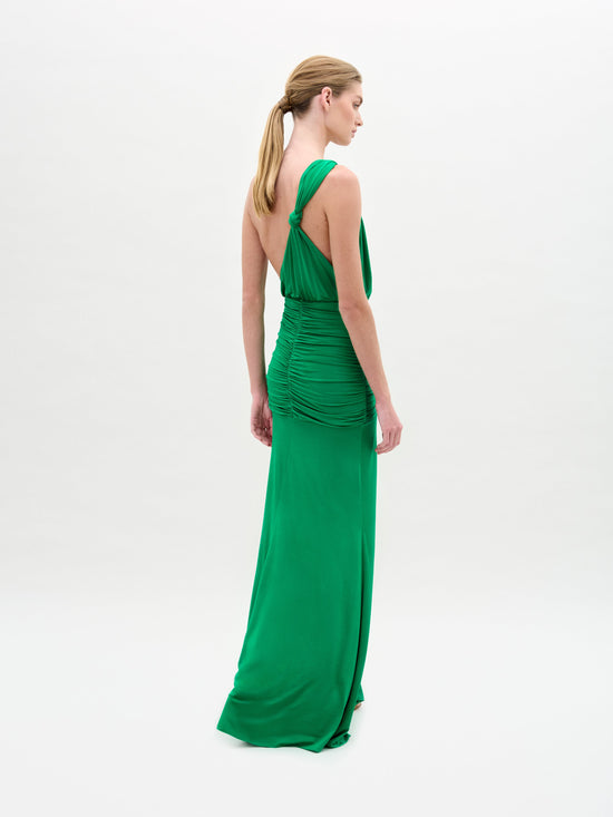 A woman in the Antara Dress, a green one-shoulder gown with a side slit, stands against a plain white background.