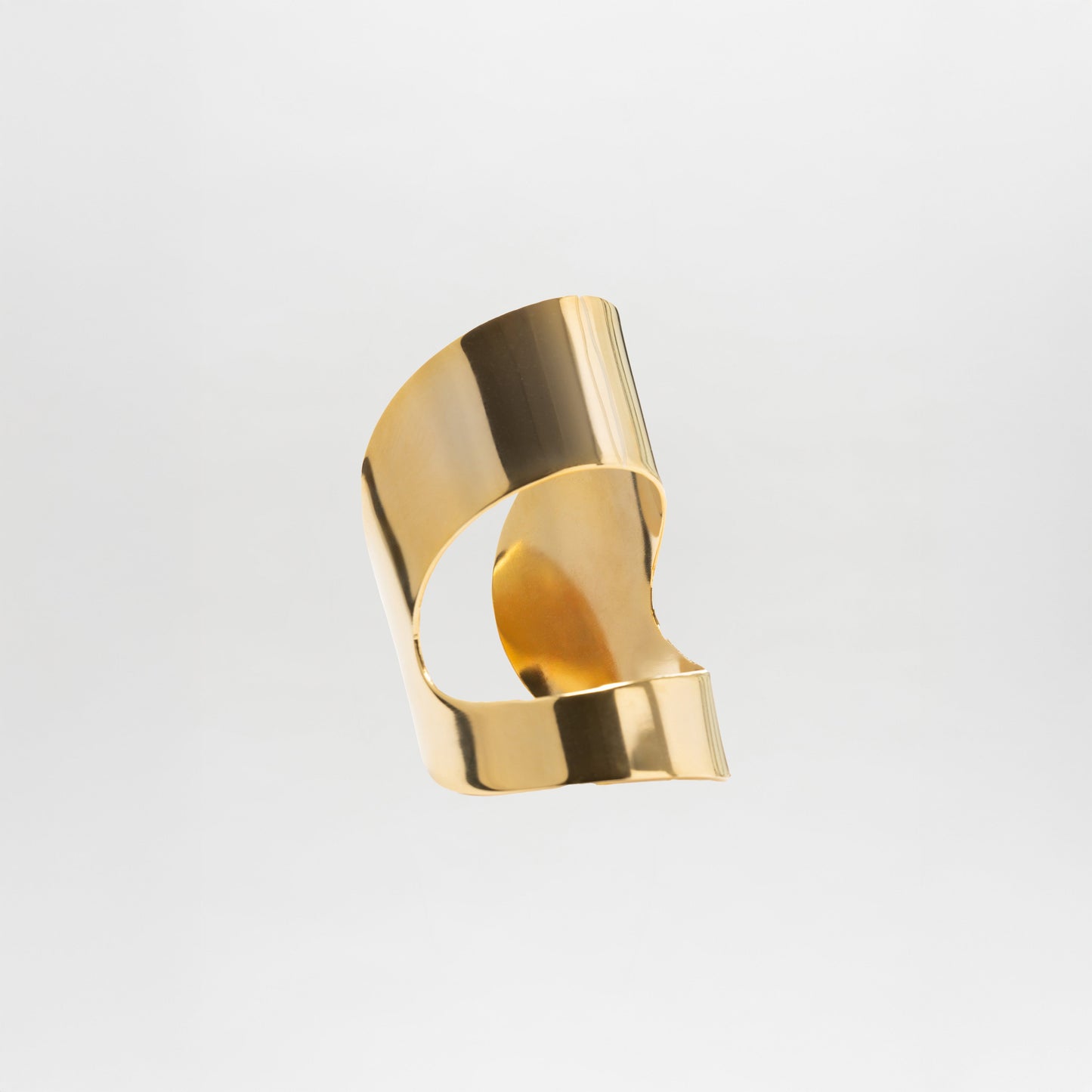 The Artemis Cuff, a shiny, abstract gold-plated brass open cuff bracelet with curved, interlocking shapes, is displayed against a plain light gray background.