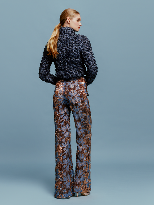 The model is wearing a blue sweater and Avellino Pant Navy Ochre Sequin available for pre-order with ship by date August 15th-September 15th.