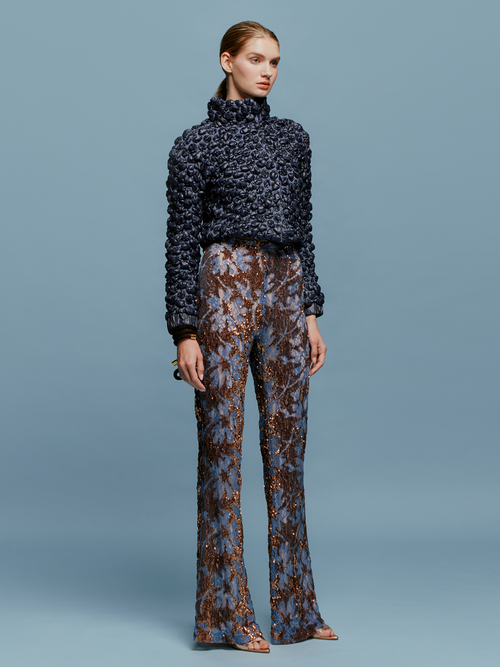 The model is wearing a blue sweater and Avellino Pant Navy Ochre Sequin available for pre-order with ship by date August 15th-September 15th.