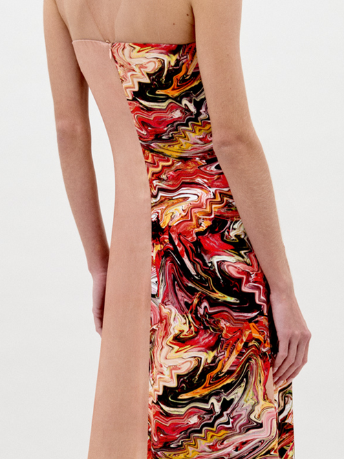 A woman stands in a long, strapless Adalgisa Dress Abstract Coral with red, orange, and yellow floral accents on the side against a plain white background. This stunning piece is available for pre-order now with an estimated ship-by date of February 1st, 2025.