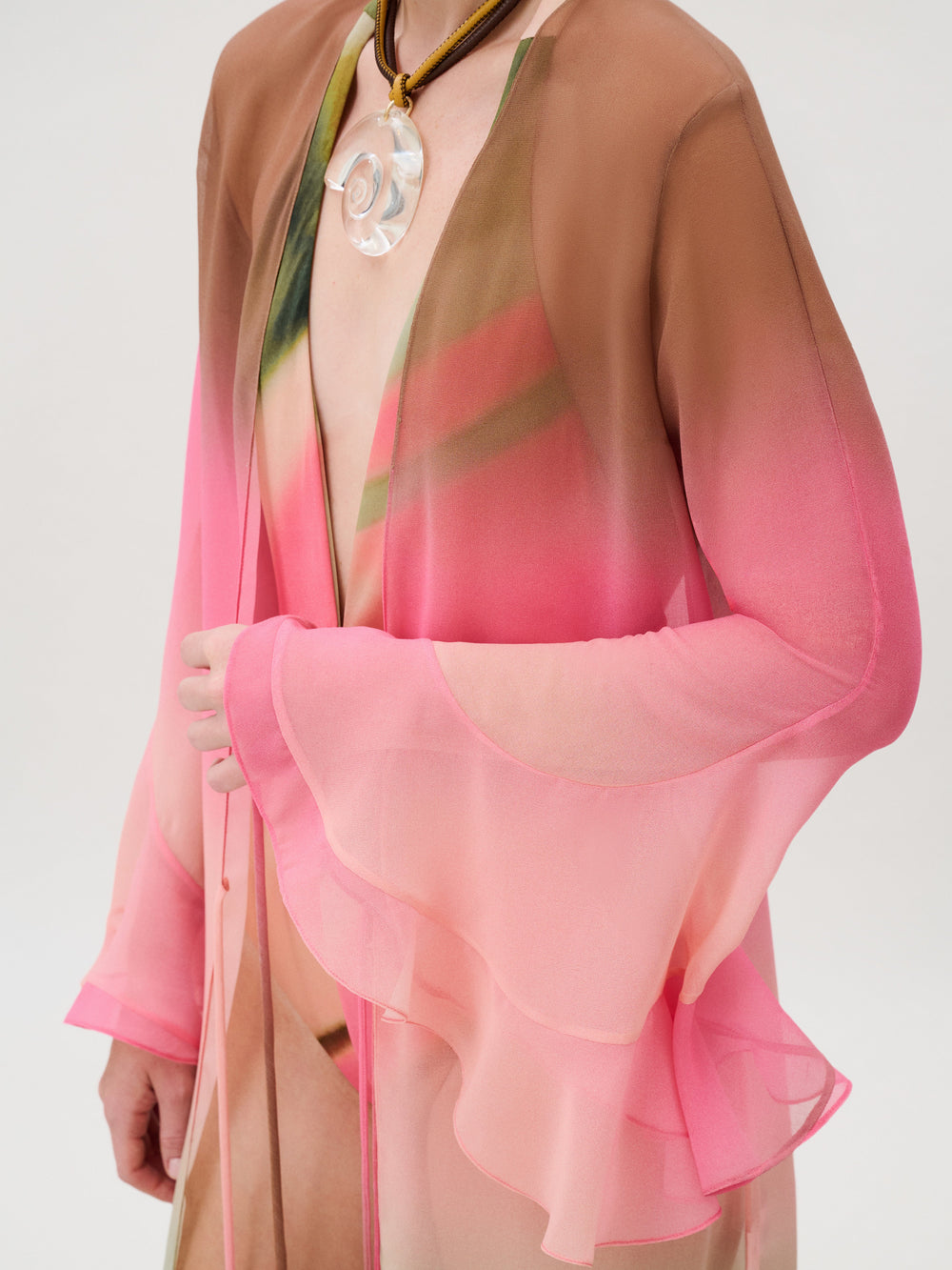 Amaris Tunic in a sheer chiffon kaftan style with ruffled sleeves in a pink and brown gradient print, worn with a large clear pendant necklace.