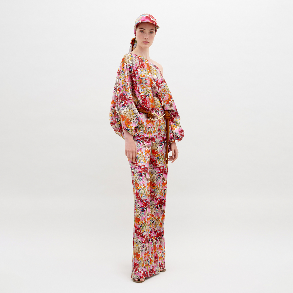 Person wearing a floral-patterned outfit consisting of an Andie Pant Multicolor Animal Print, a one-shoulder top, and a matching cap, standing against a plain white background. This stunning ensemble is now available for pre-order with an expected ship date of November 15th, 2024.