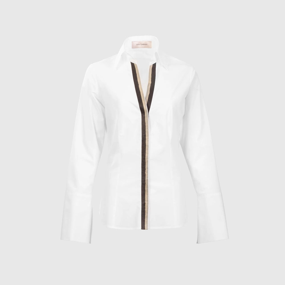 The Andrea Blouse is a white, long-sleeve top crafted from 100% cotton Portuguese fabric, with wide cuffs and a brown vertical stripe down the front center, shown against a plain light gray background.