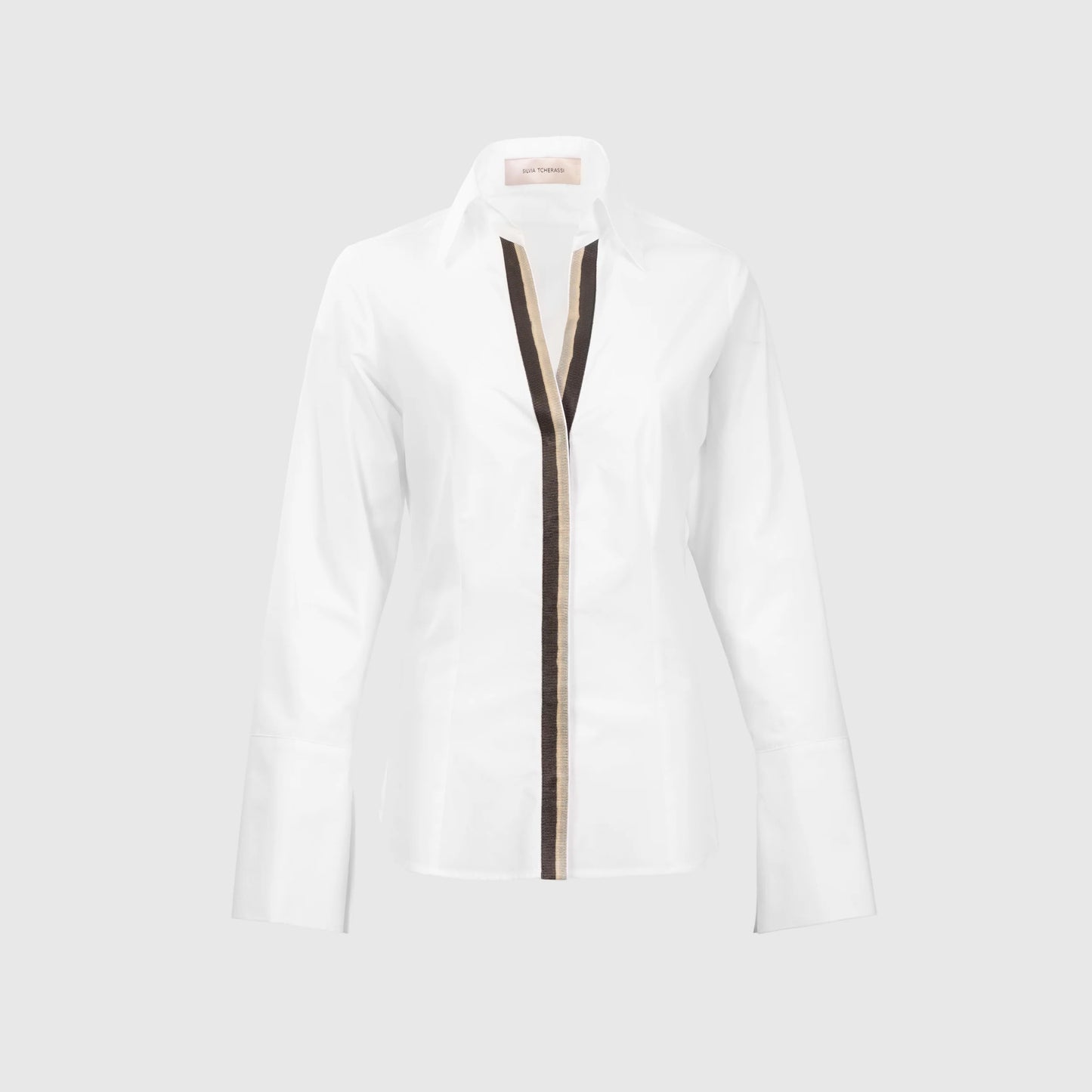 The Andrea Blouse is a white, long-sleeve top crafted from 100% cotton Portuguese fabric, with wide cuffs and a brown vertical stripe down the front center, shown against a plain light gray background.