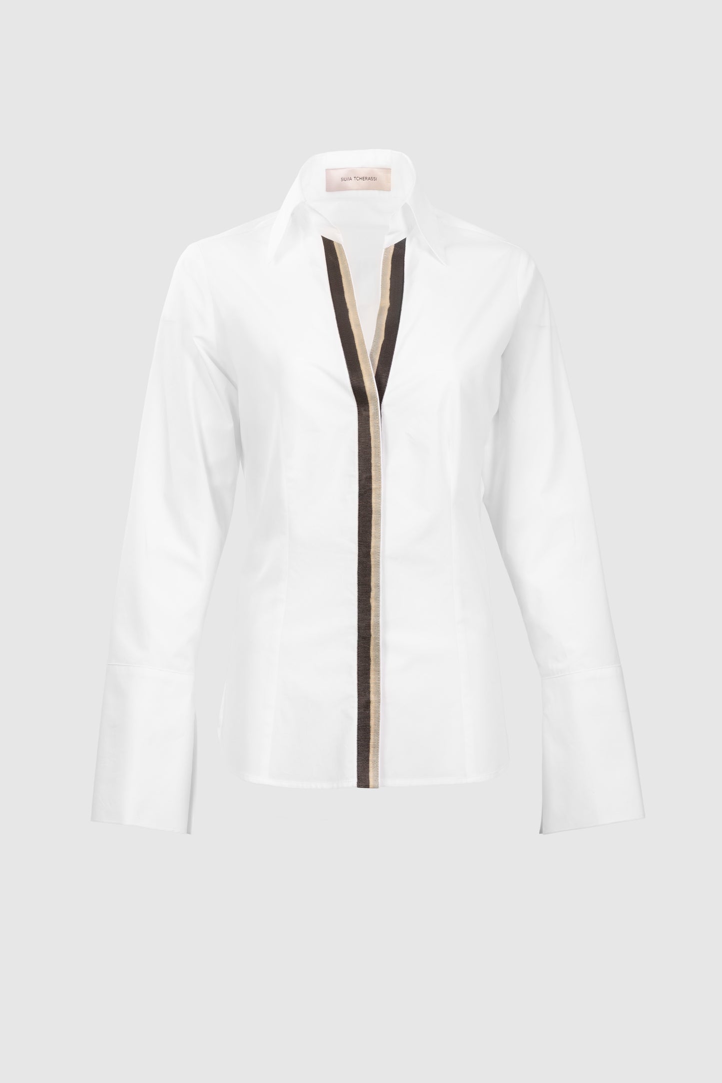 The Andrea Blouse is a white, long-sleeve, collared shirt made from 100% Portuguese cotton, featuring a black and beige vertical front stripe. Shown on a light grey background.