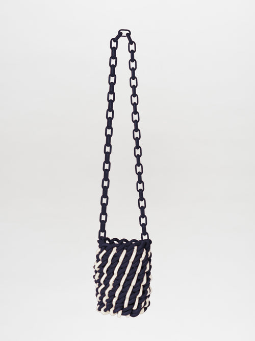 The Anise Bag Navy White is a woven handbag with a chain strap, featuring a navy and white spiral design.