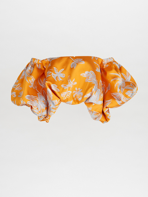 The Arezzo Blouse Apricot Silver showcases a charming orange off-the-shoulder design with a white floral pattern and voluminous sleeves, exuding polished elegance against a plain background.