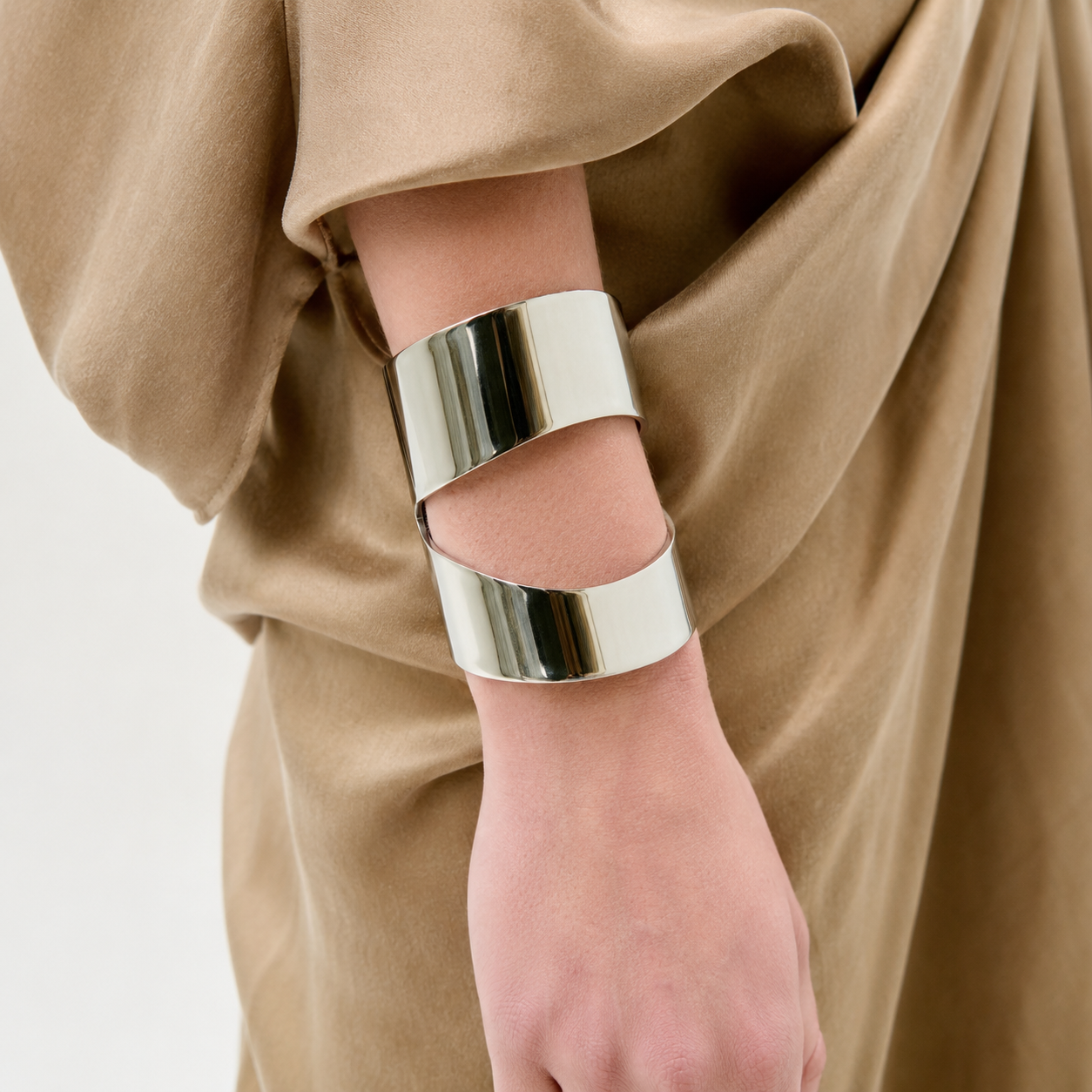 A person wears a camel-colored draped garment and the Artemis Cuff—a wide, modern silver bracelet with a unique overlapping open design—on their wrist.
