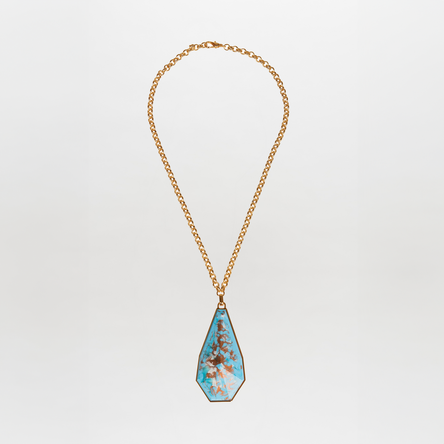 The Ascoli Necklace by Tcherassi showcases a gold chain with a large teardrop-shaped turquoise fantasy stone pendant, accentuated by brown veining and set in an elegant metallic frame against a white background.