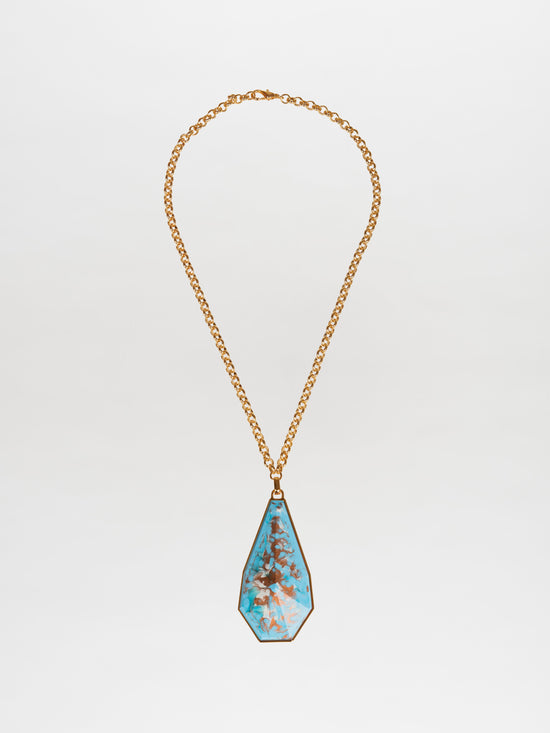 The Ascoli Necklace Aqua features a gold necklace with a large, teardrop-shaped turquoise pendant adorned with a tree-like pattern, masterfully crafted in gold plated brass. This stunning design by Tcherassi beautifully combines elegance and artistry.