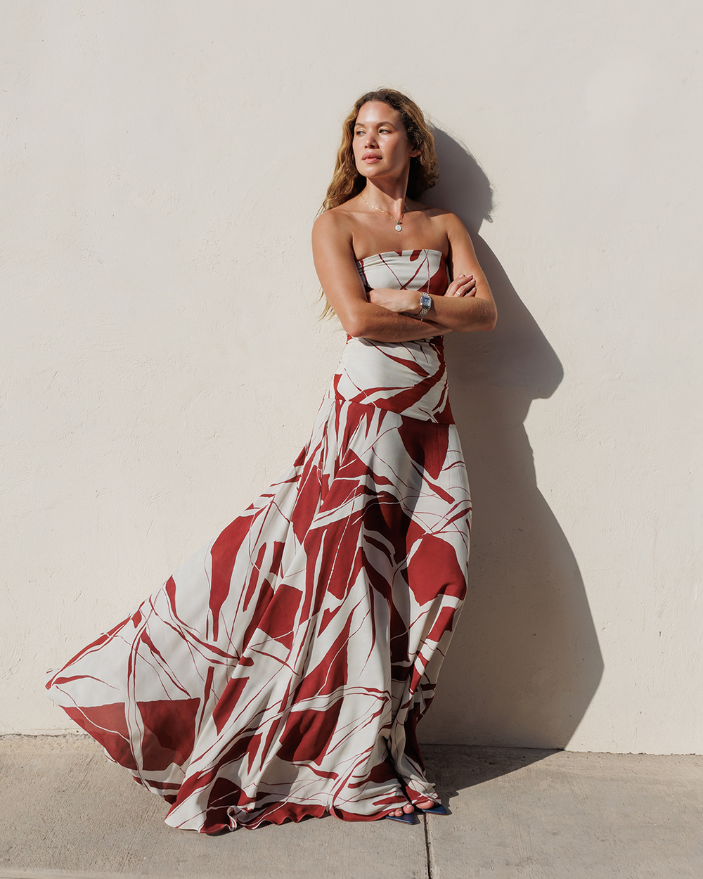 Woman wearing a strapless red and white patterned dress against a light wall.