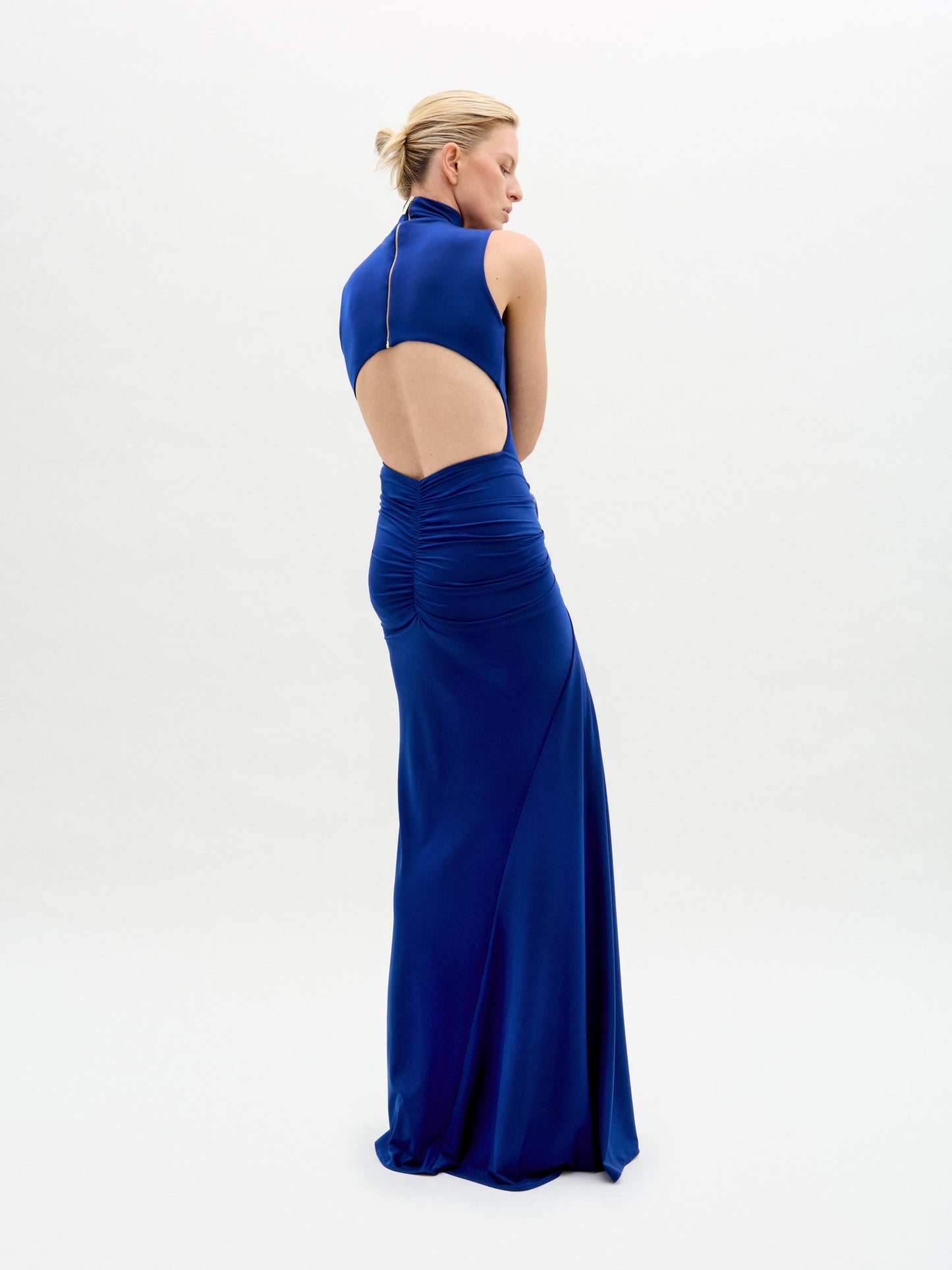 A model wears the Bogna Dress, a sleeveless high-neck blue gown with draped detail, against a plain white background.