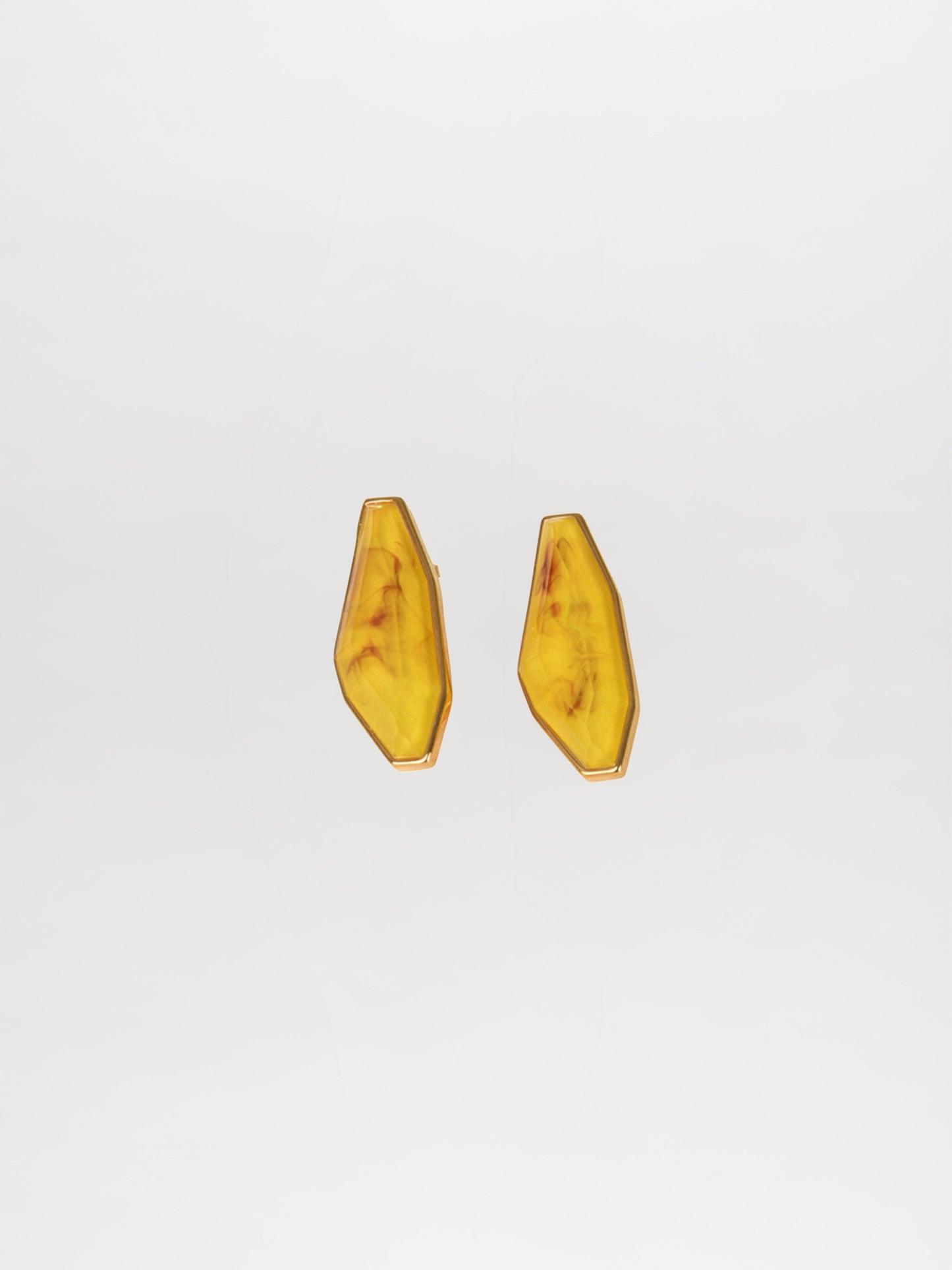 The Badra Earrings Marigold, crafted with Italian resin, feature a striking marbled amber pattern set in geometric gold shapes, all elegantly displayed against a plain white background.