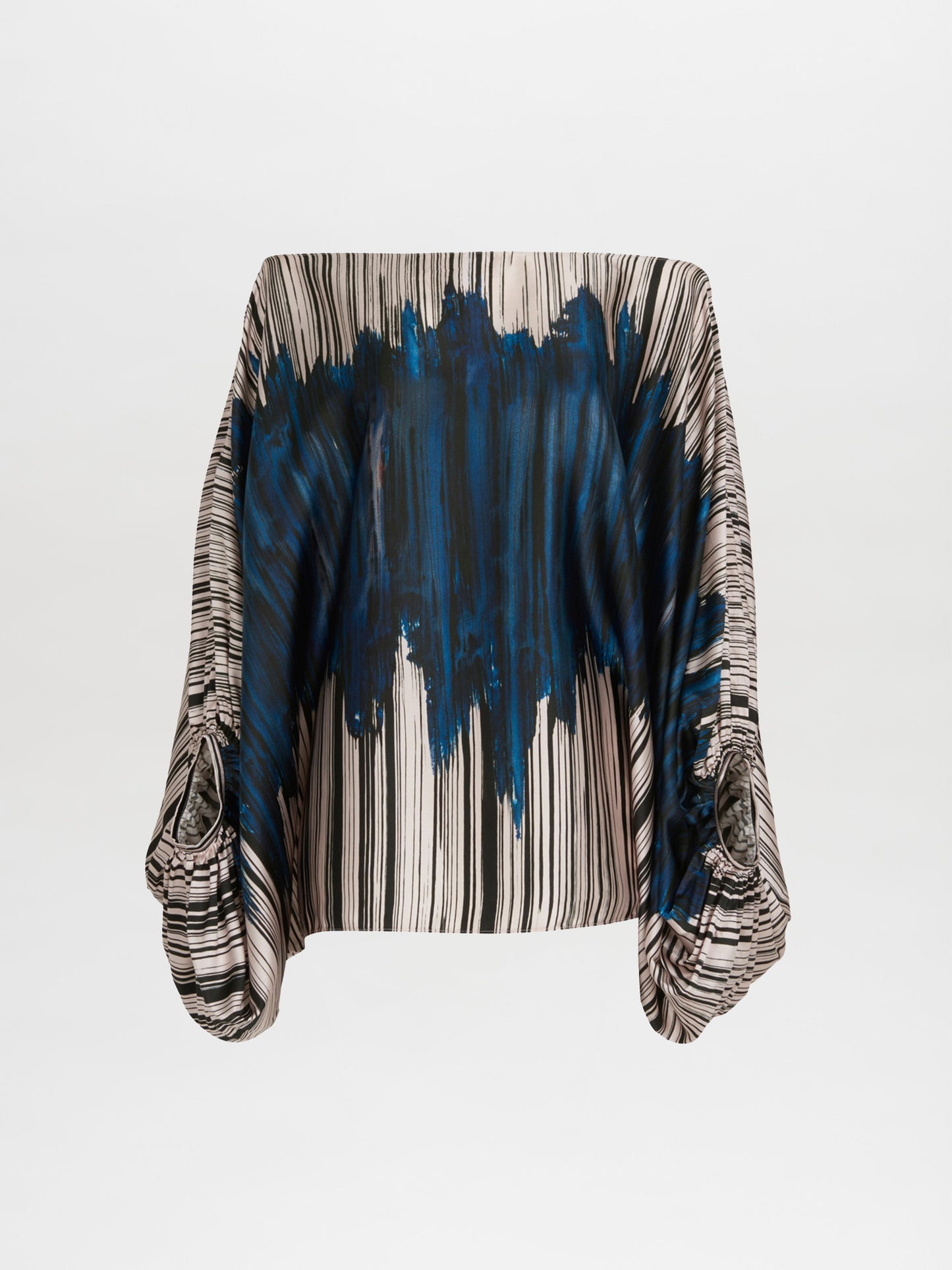 The Bellagio Blouse Indigo Linear, a versatile silk blouse from the Fall 2023 collection, features long draped sleeves with vertical black and white stripes and a bold blue splash design in the center.