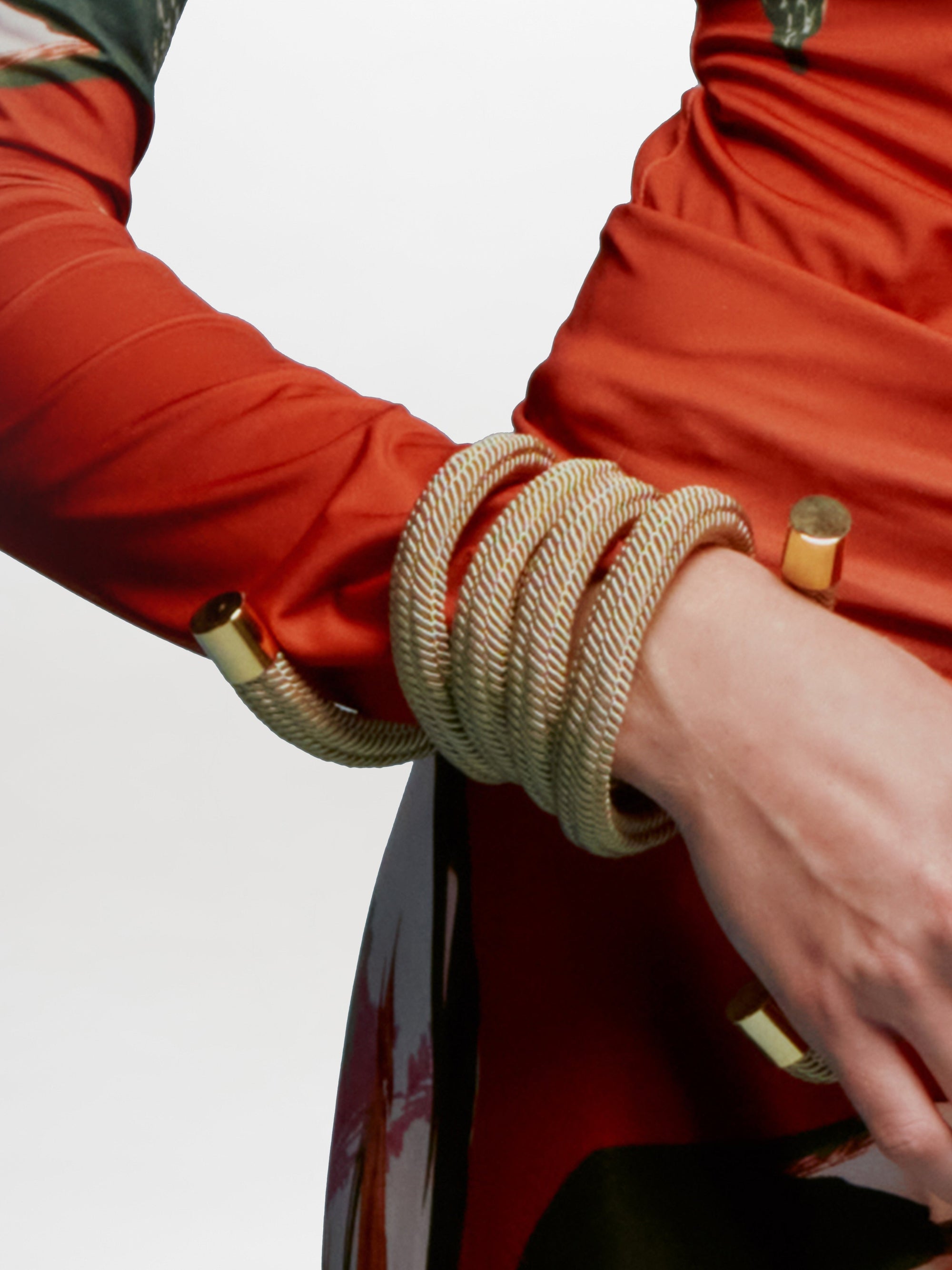 The Nicky Bracelet, crafted from gold-plated brass, exhibits a spiral-shaped pendant with a textured metallic finish and gold accents. It features an elegant hanging "S" charm, embodying elegance and sophistication in Tcherassi's design.