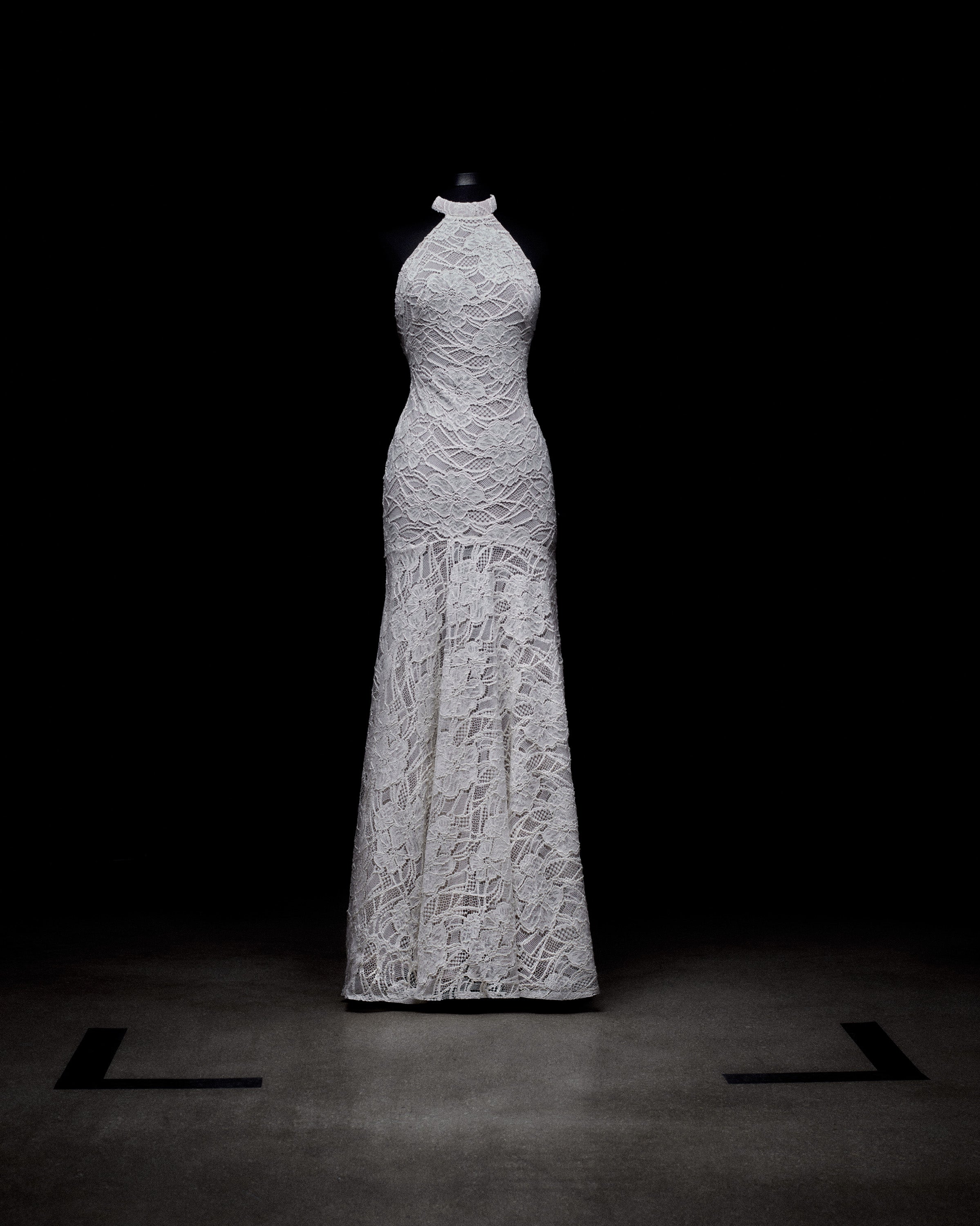 White lace evening gown on a mannequin against a dark background.