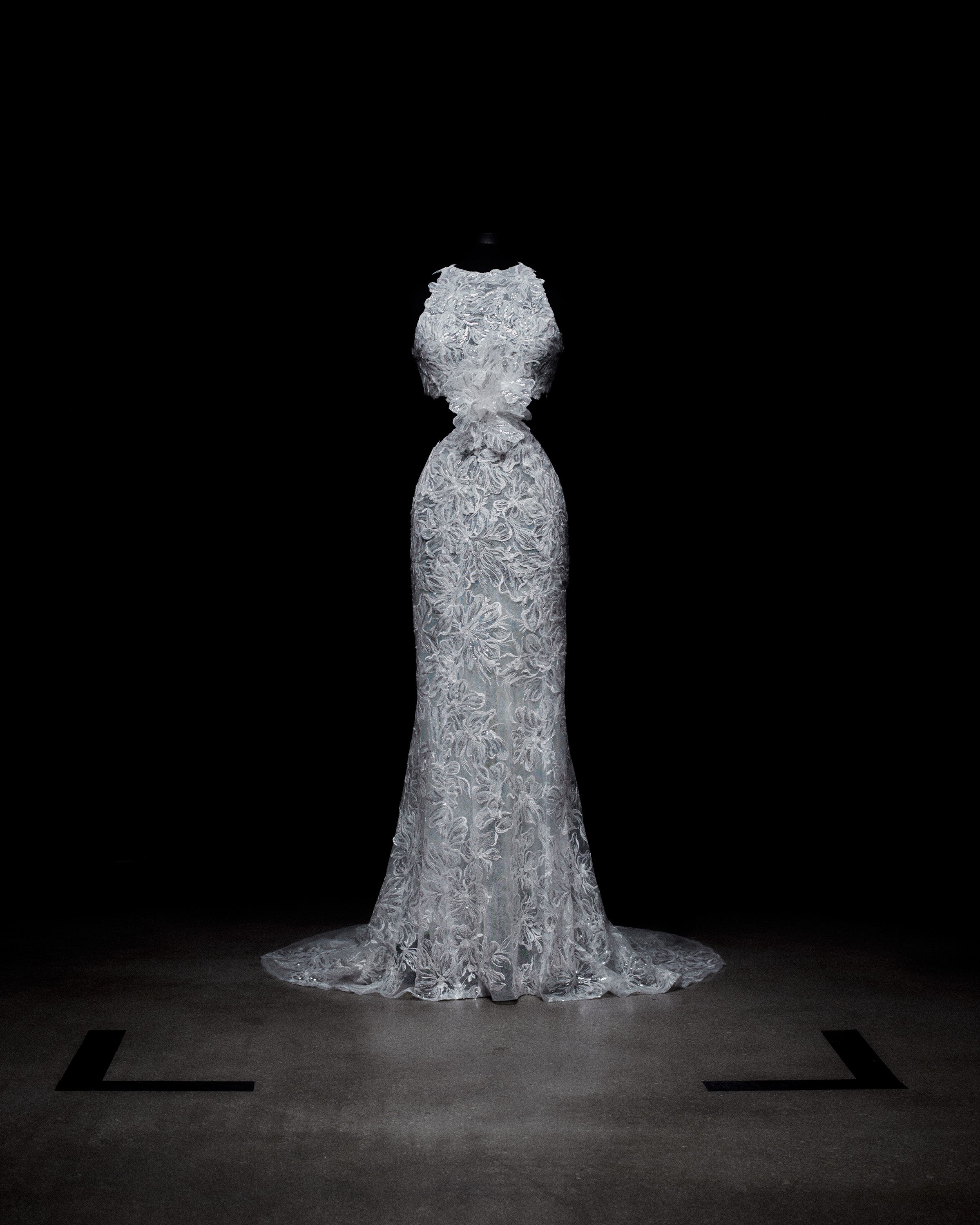 A white lace wedding dress on a mannequin, displayed against a dark background.