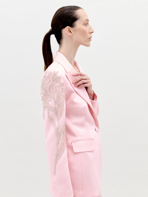 Profile view of a person with long hair tied back, wearing the Rebeca Jacket Pink, a light pink blazer adorned with intricate embroidery on the shoulder; pre-order now for delivery by February 1st, 2025.